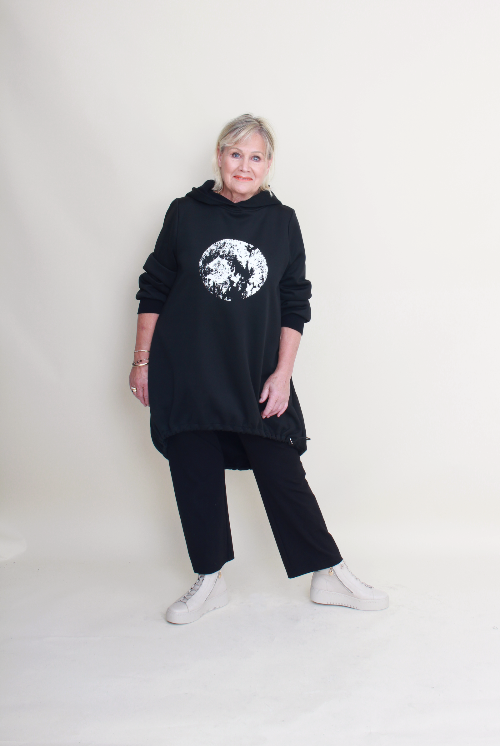 Person wearing a black hoodie with a graphic design on a plain background