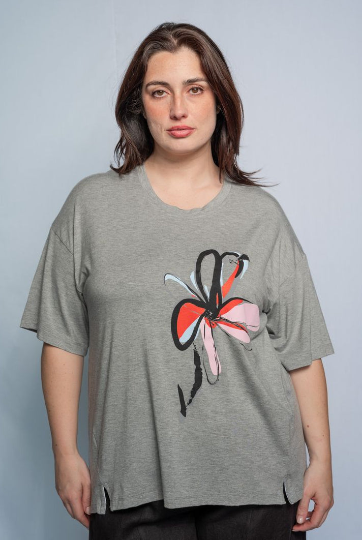 Woman wearing a grey t shirt with flower motif and black pants against a white background.
