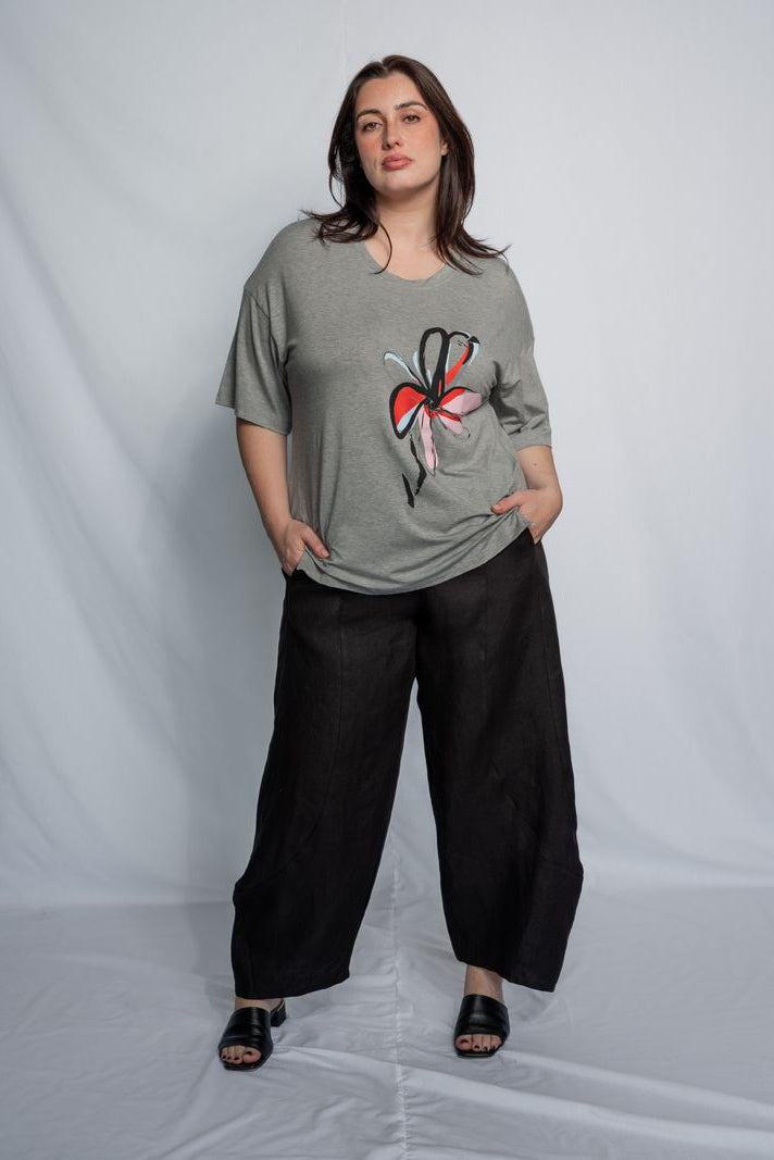 Woman wearing a grey t shirt with flower motif and black pants against a white background.