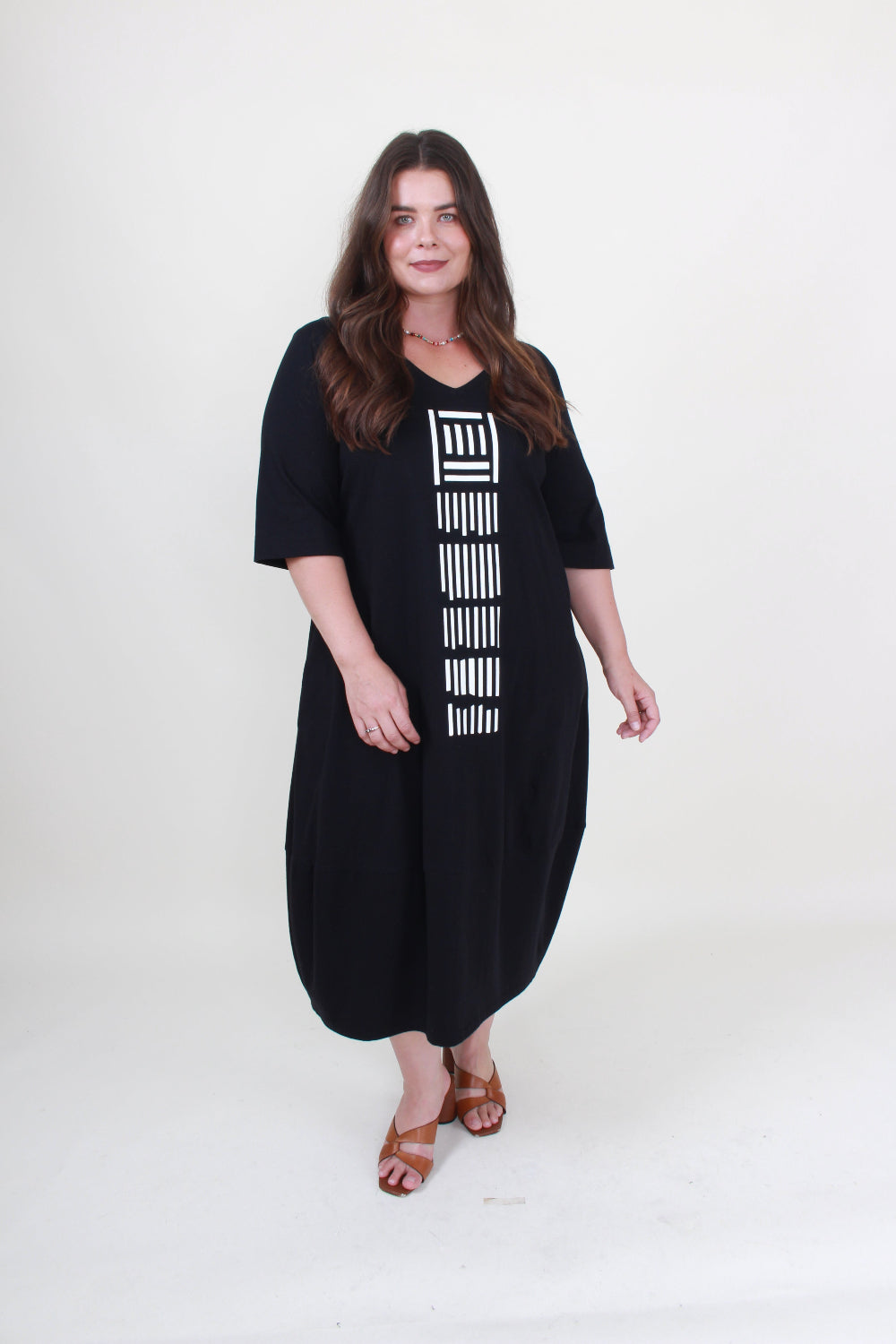 lady in black cocoon dress with white graphic down the front on plain background