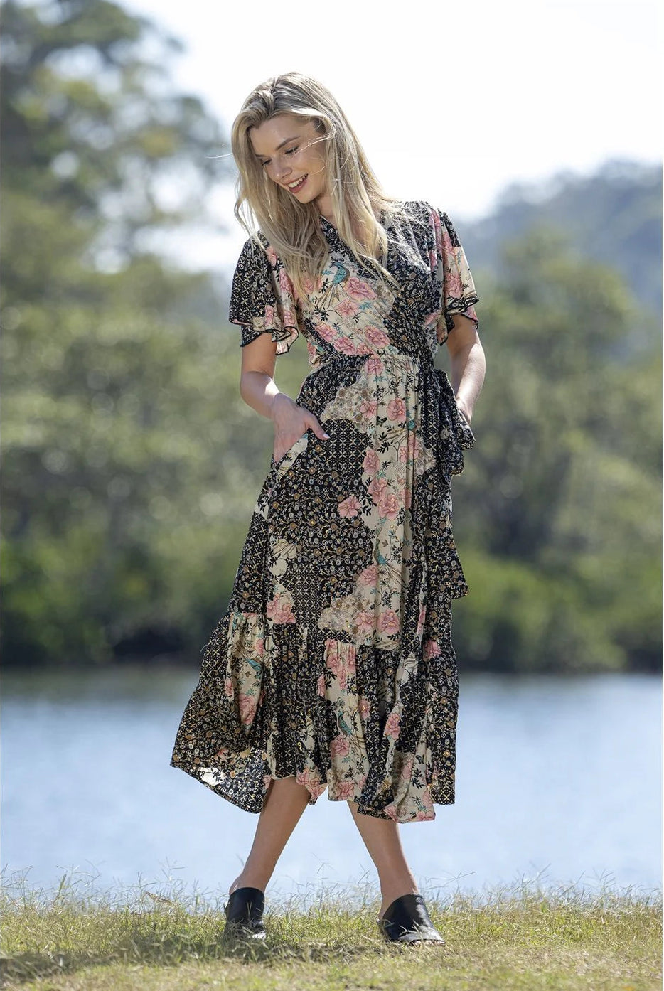 Woman in a floral dress standing by a lake with trees in the background