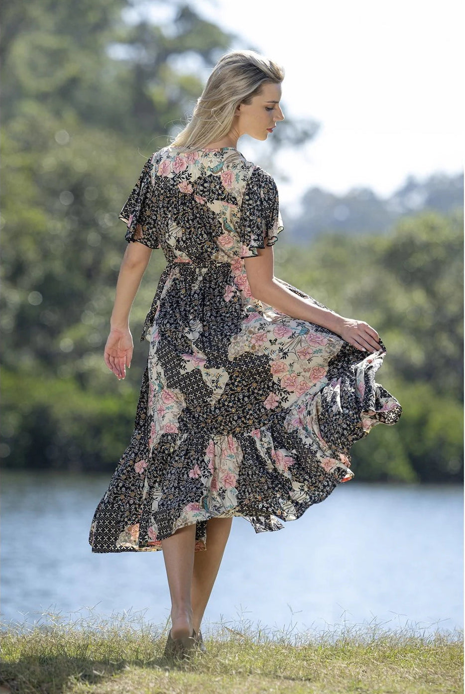 Woman in a floral dress standing by a lake with trees in the background