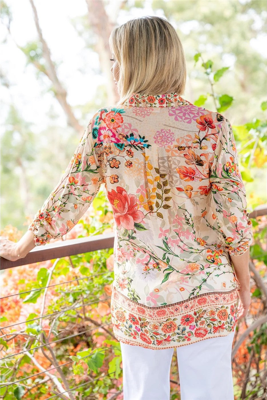 Woman wearing a floral blouse standing outdoors with trees in the background