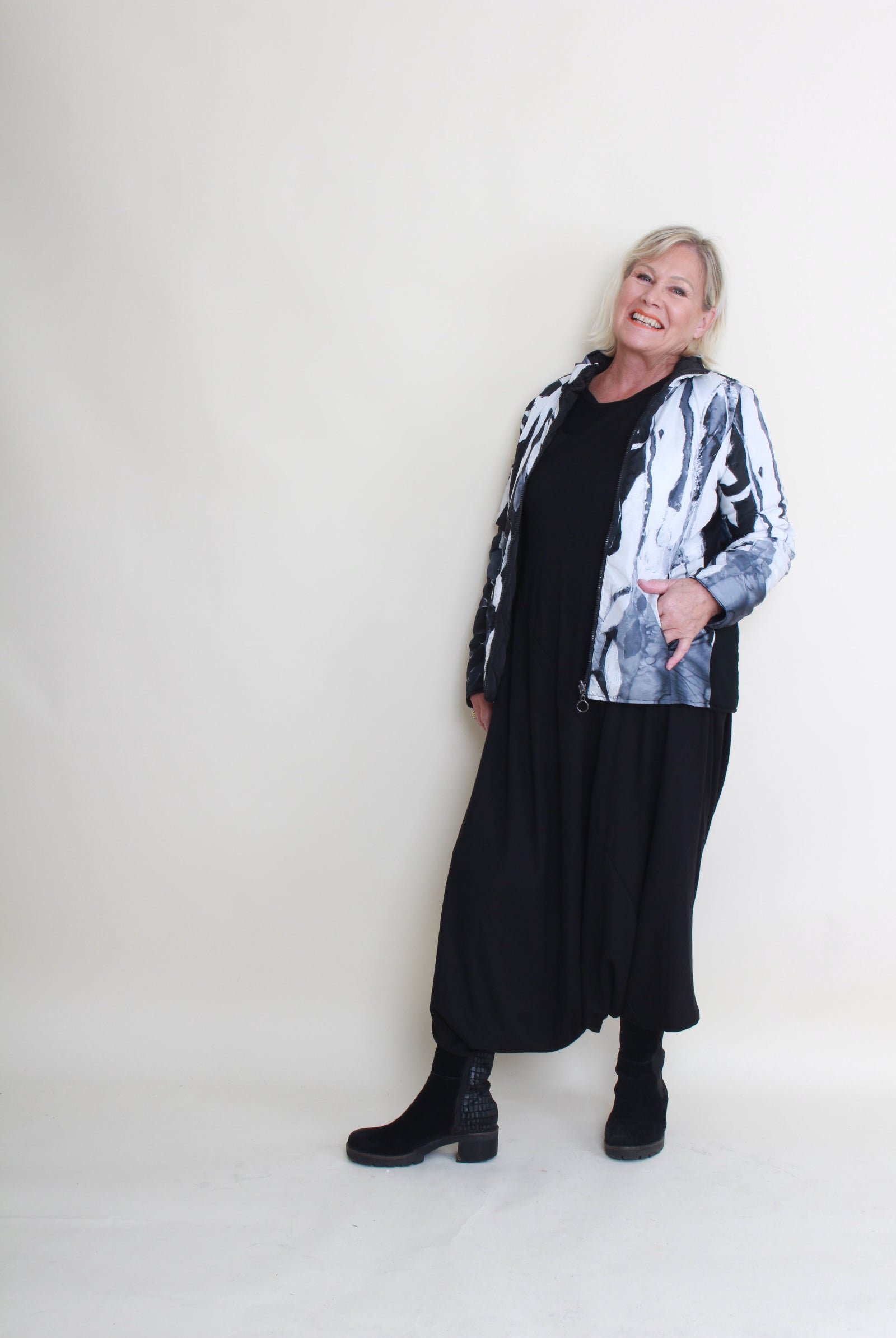 Woman wearing a black and white patterned jacket with a black dress against a white background