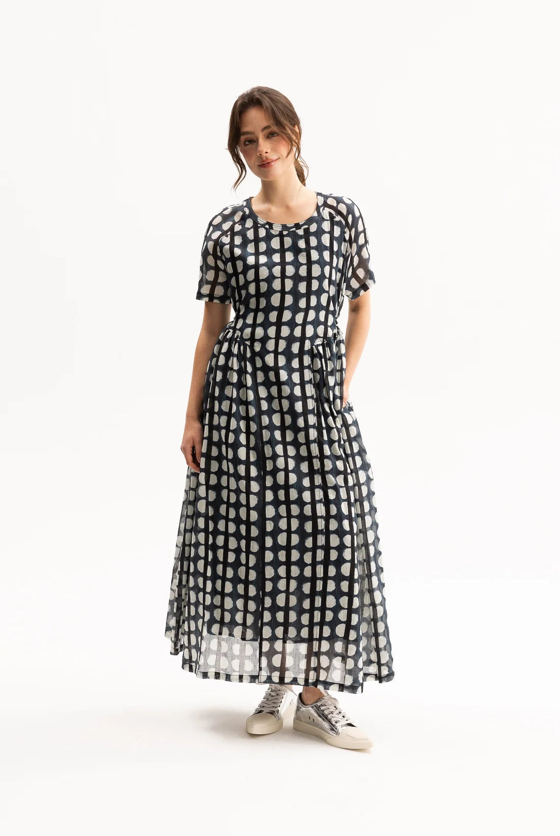 A woman modeling a short-sleeve midi dress with a black and white polka dot pattern, standing against a plain white studio background.
