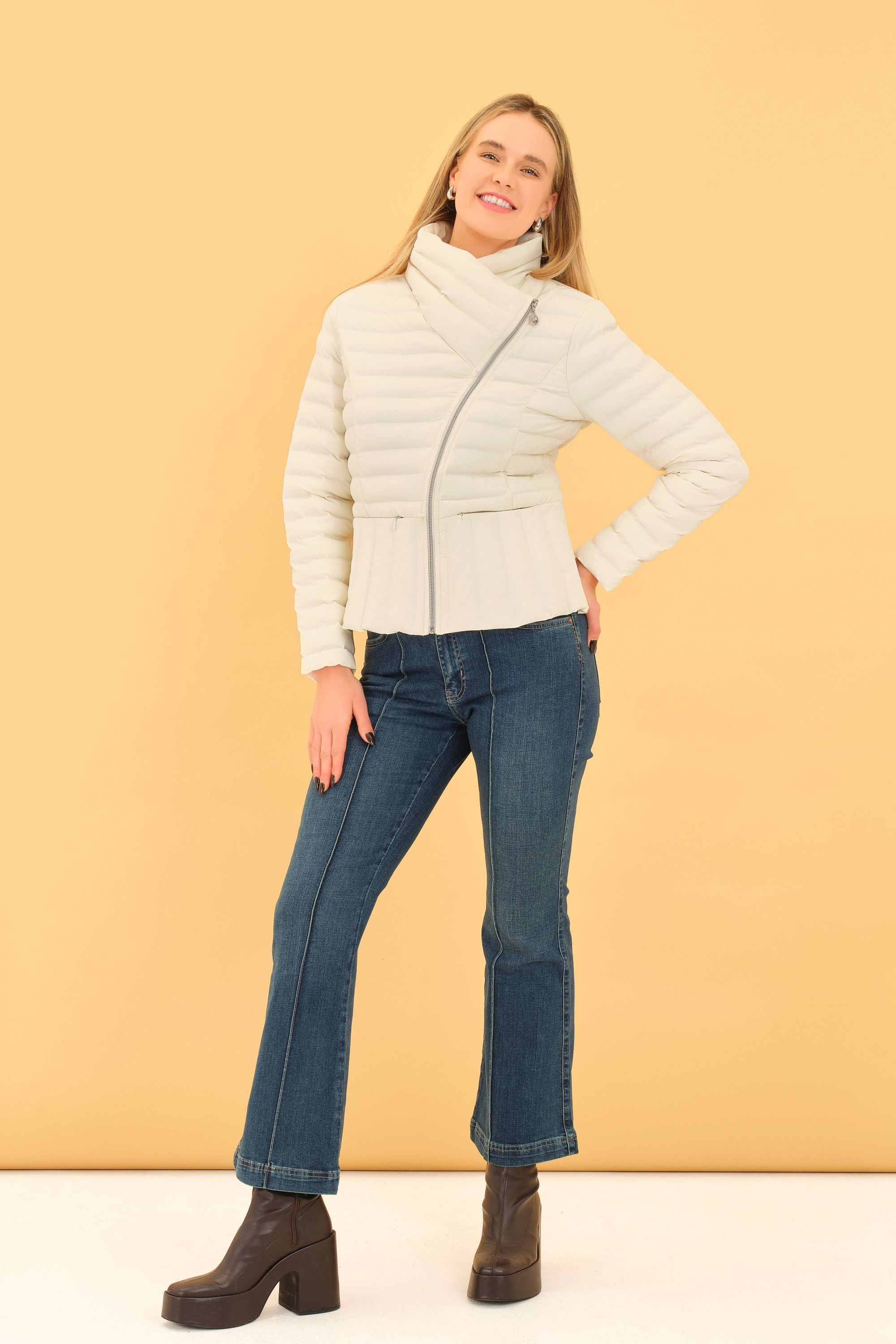 Woman wearing a white puffer jacket and blue jeans against a yellow background