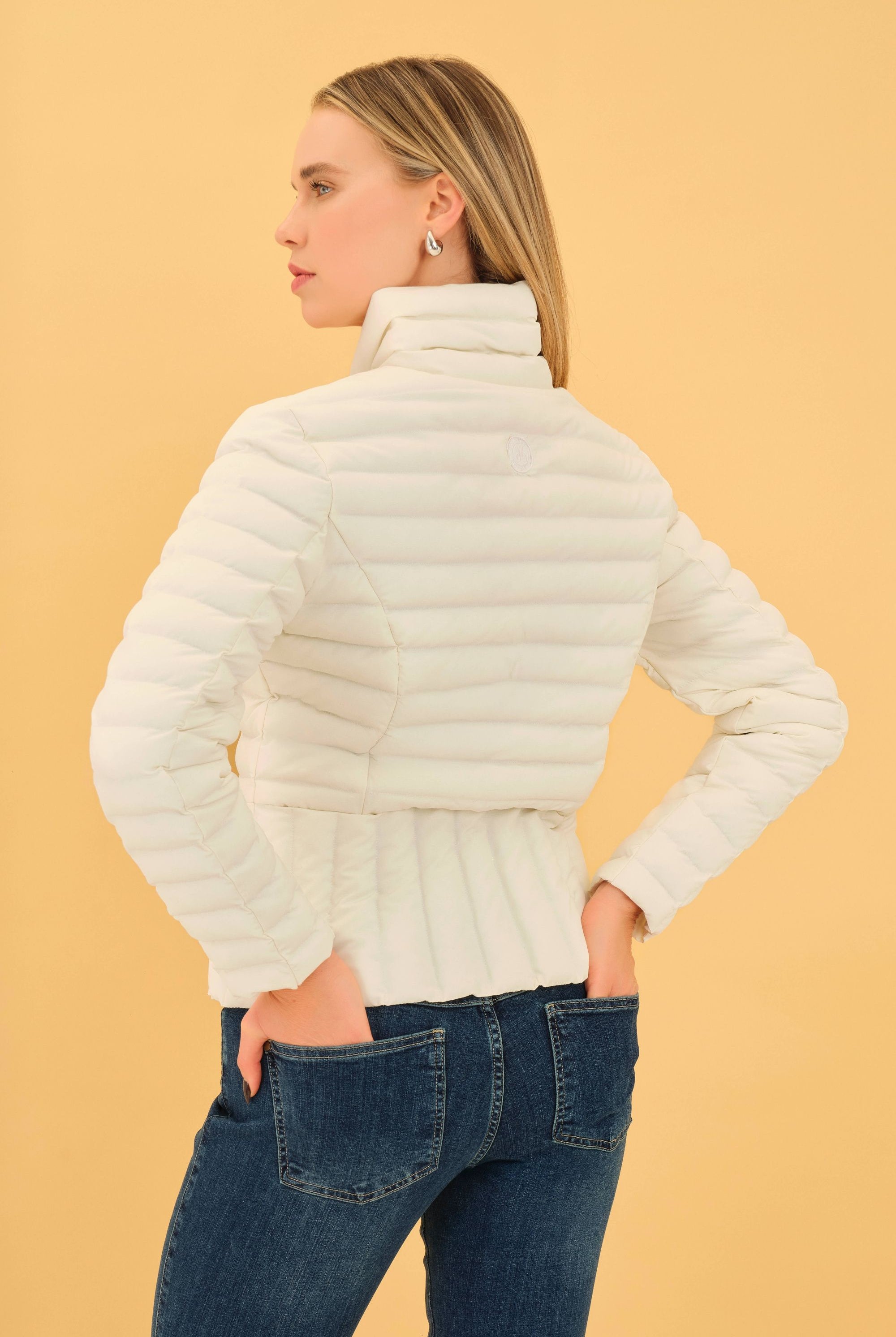 Woman wearing a cream puffer jacket against a beige background back angle