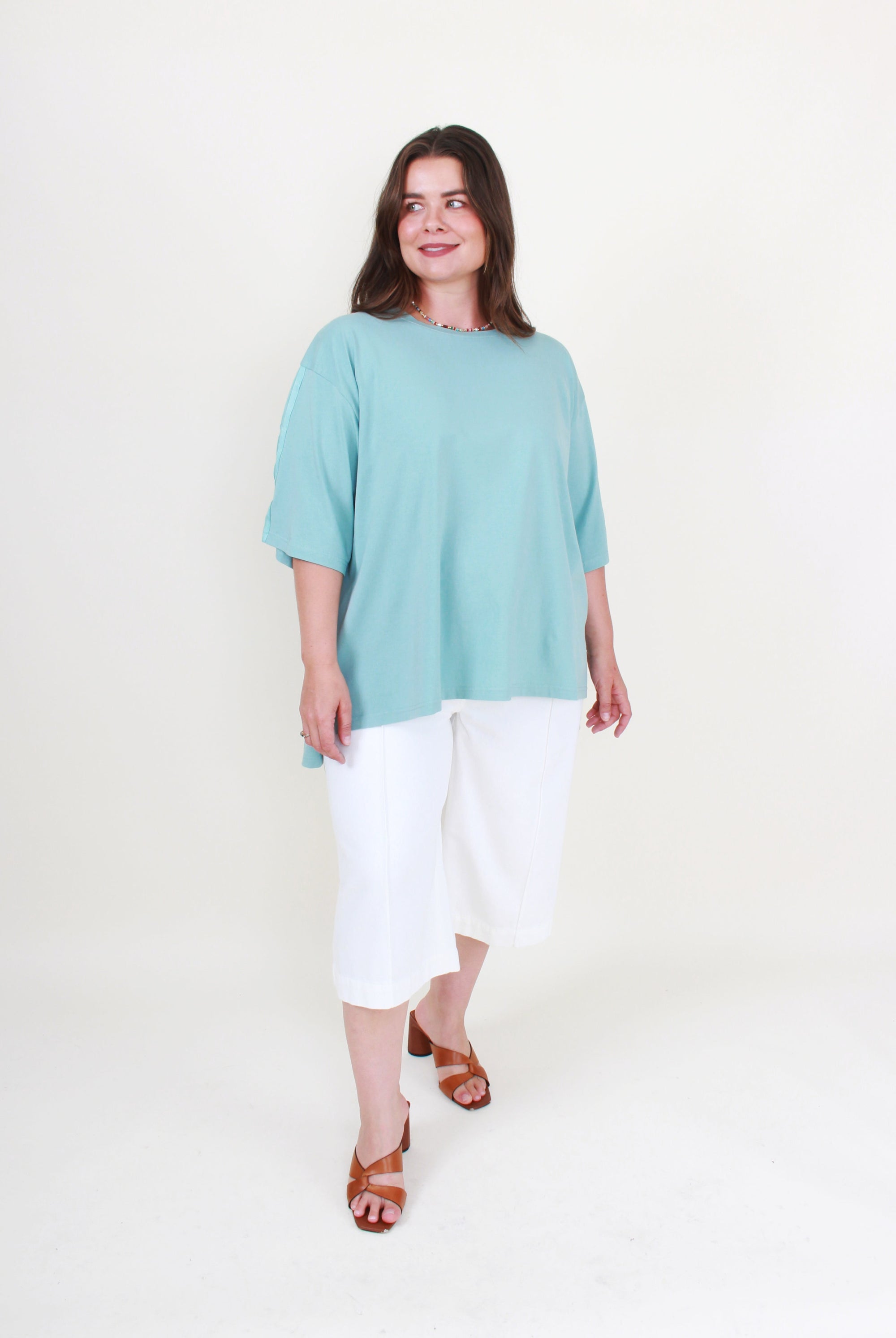 Woman wearing a light blue top and white pants on a white background