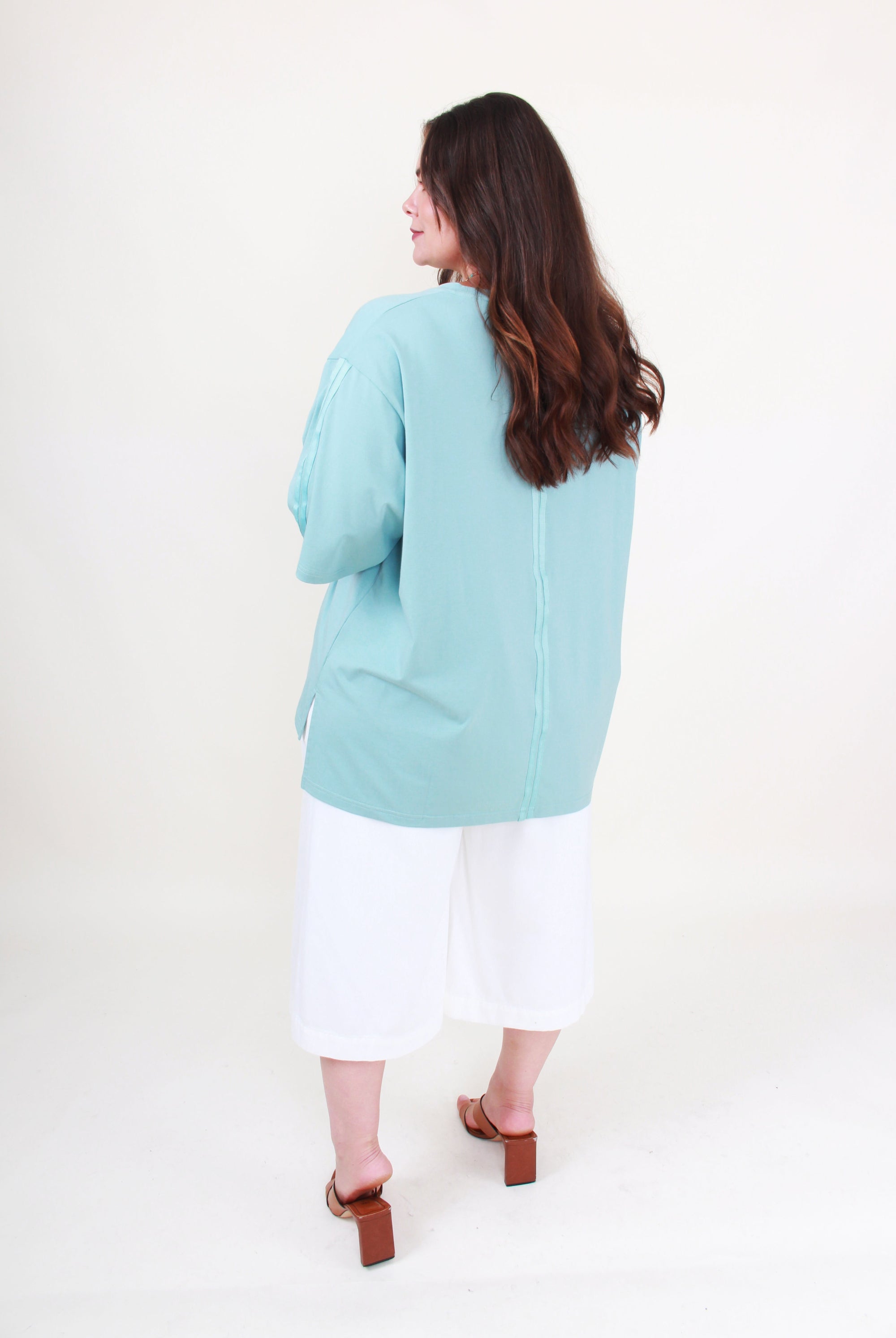 Woman wearing a light blue top on a white background back view