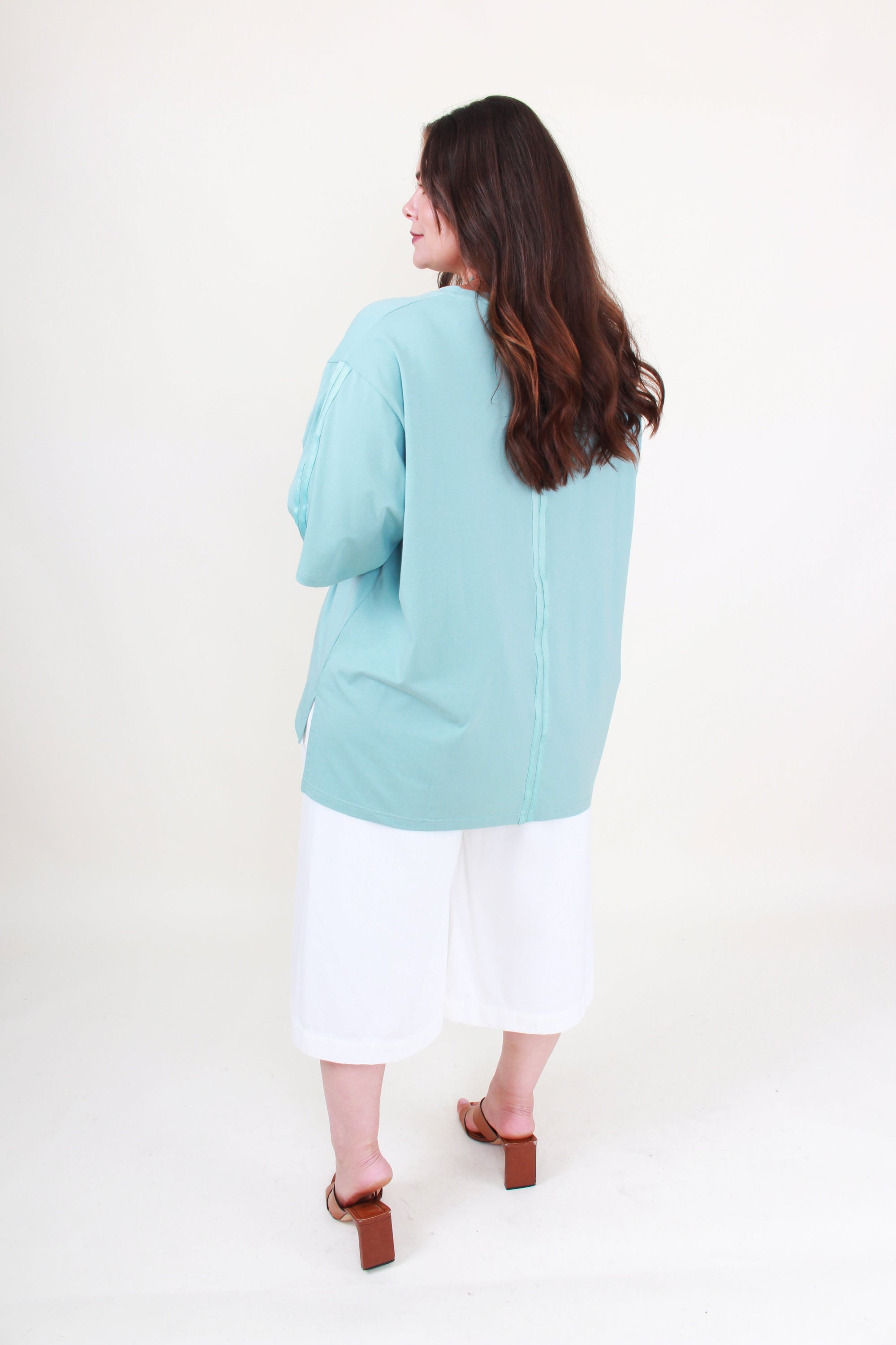 Woman wearing a light blue top on a white background back view
