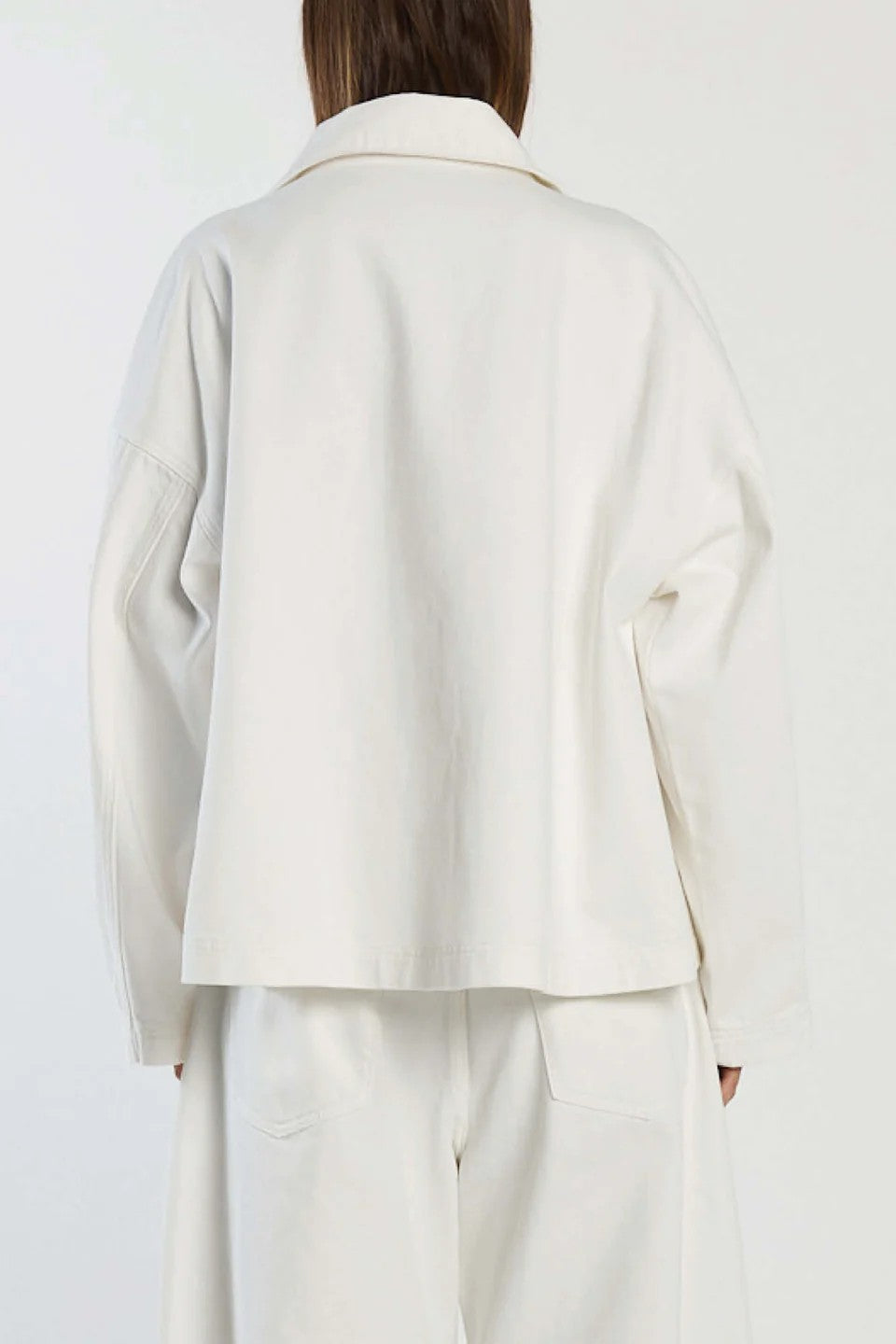 Person wearing a white coat and pants on a plain background back view