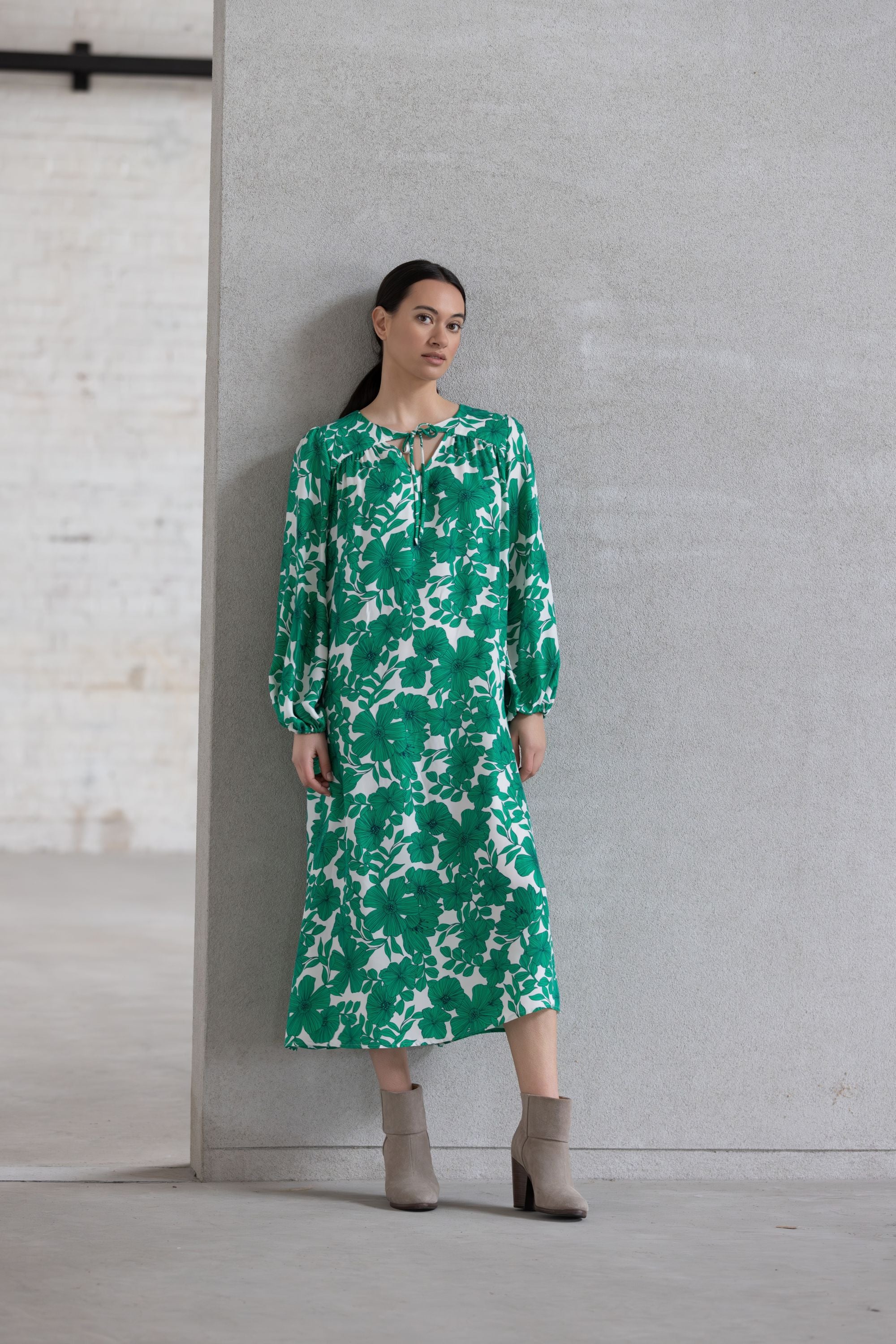 Woman wearing a green floral dress against a gray wall.