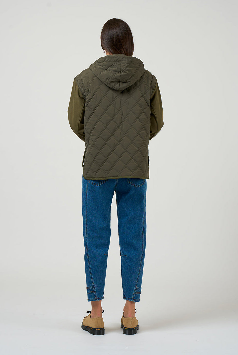 Person wearing a green quilted jacket and blue jeans on a white background