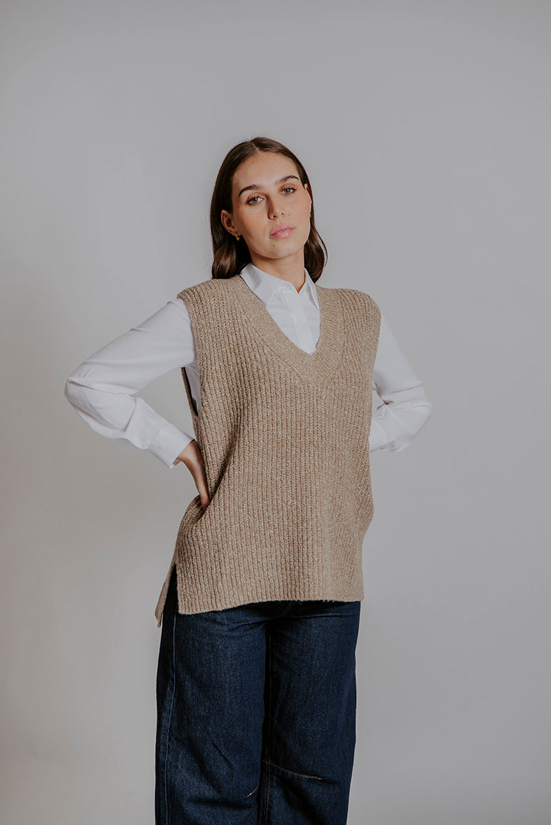 Woman wearing a beige knitted vest over a white shirt with a plain background