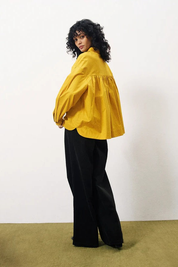 Person wearing a yellow blouse and black pants on a white background back view