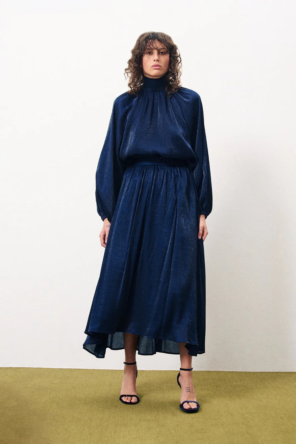 Woman wearing a navy blue dress standing on a green carpet with a white wall background