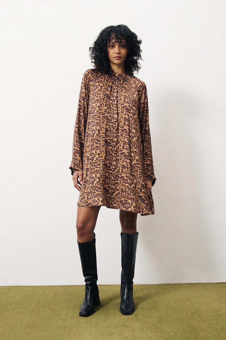 Woman wearing a leopard print dress and black knee-high boots against a white background