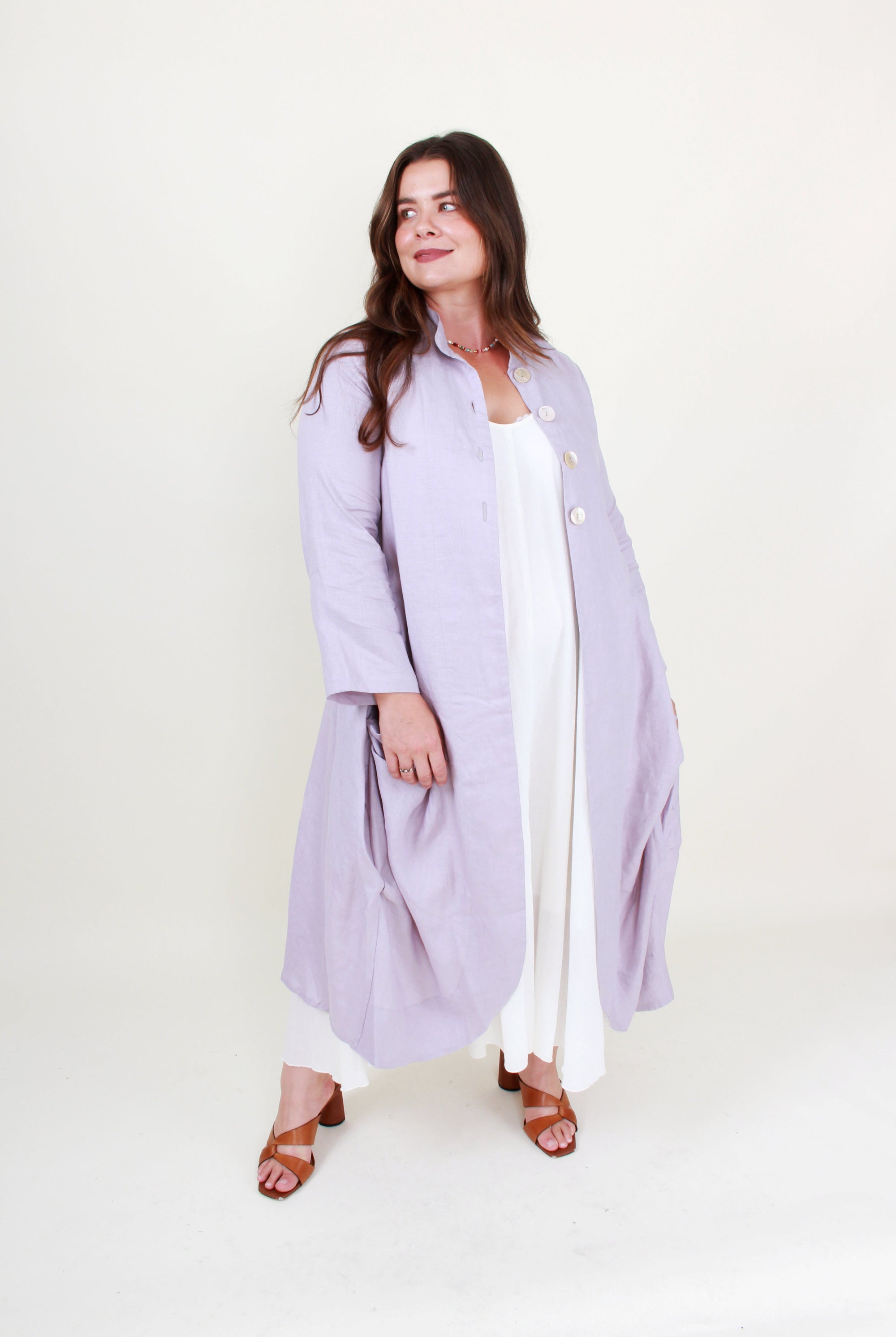 Woman wearing a light purple coat over a white dress on a white background