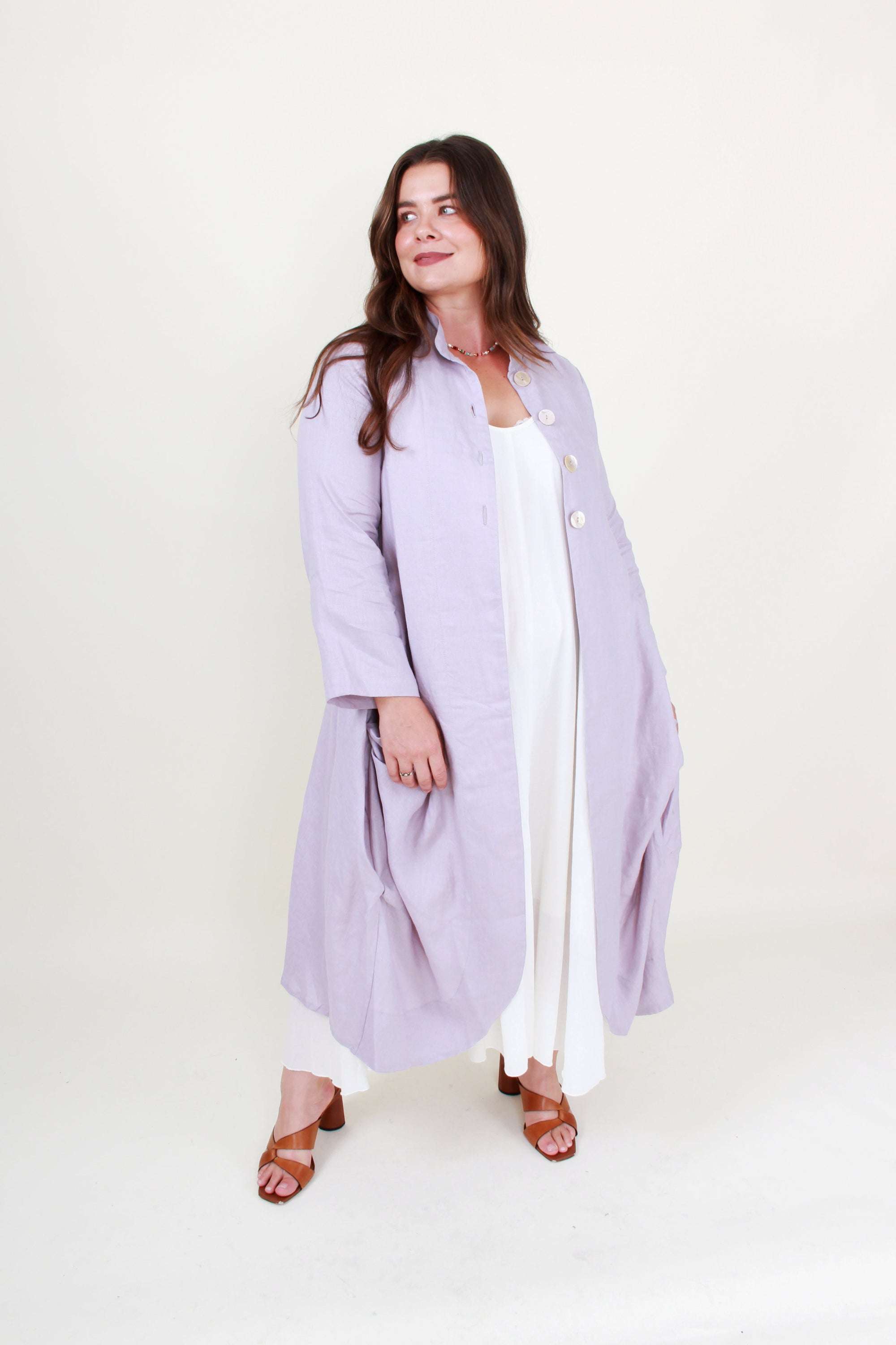 Woman wearing a light purple coat over a white dress on a white background
