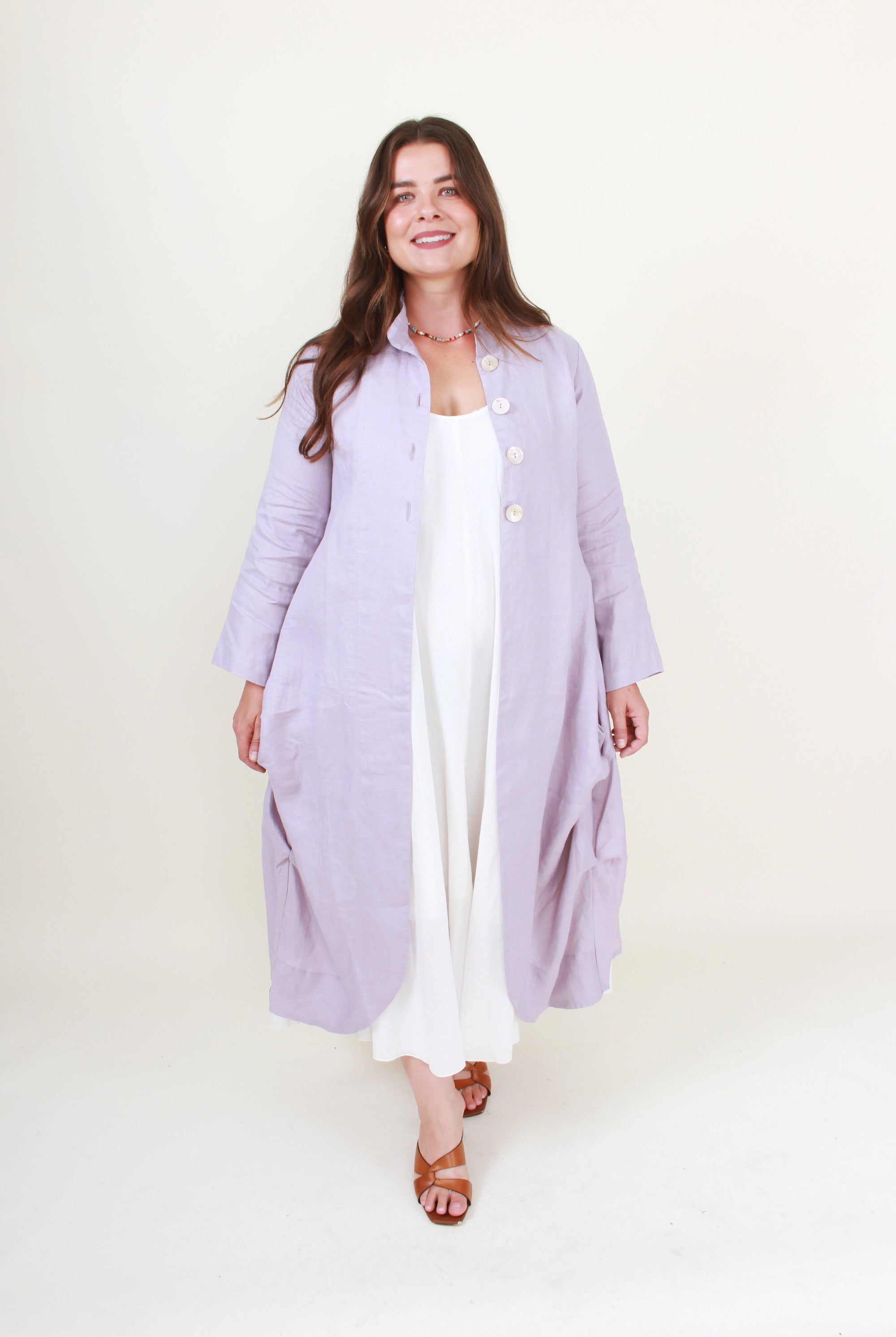 Woman wearing a long light purple coat over a white outfit on a white background