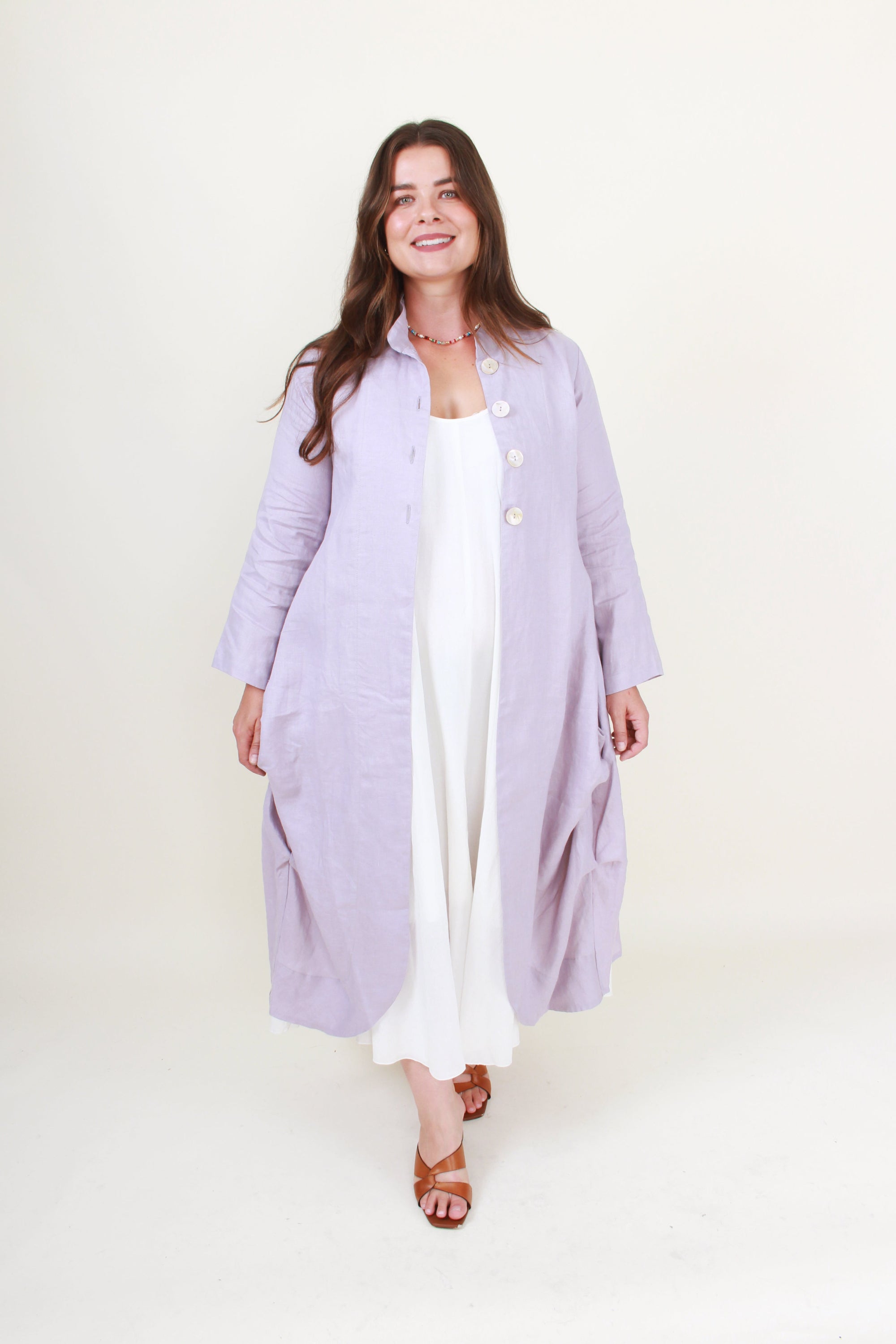 Woman wearing a long light purple coat over a white outfit on a white background