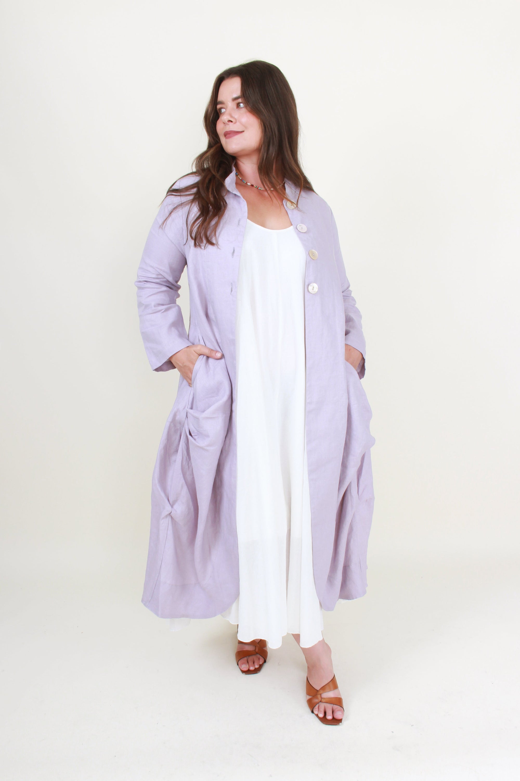 Woman wearing a long light purple coat over a white outfit on a white background