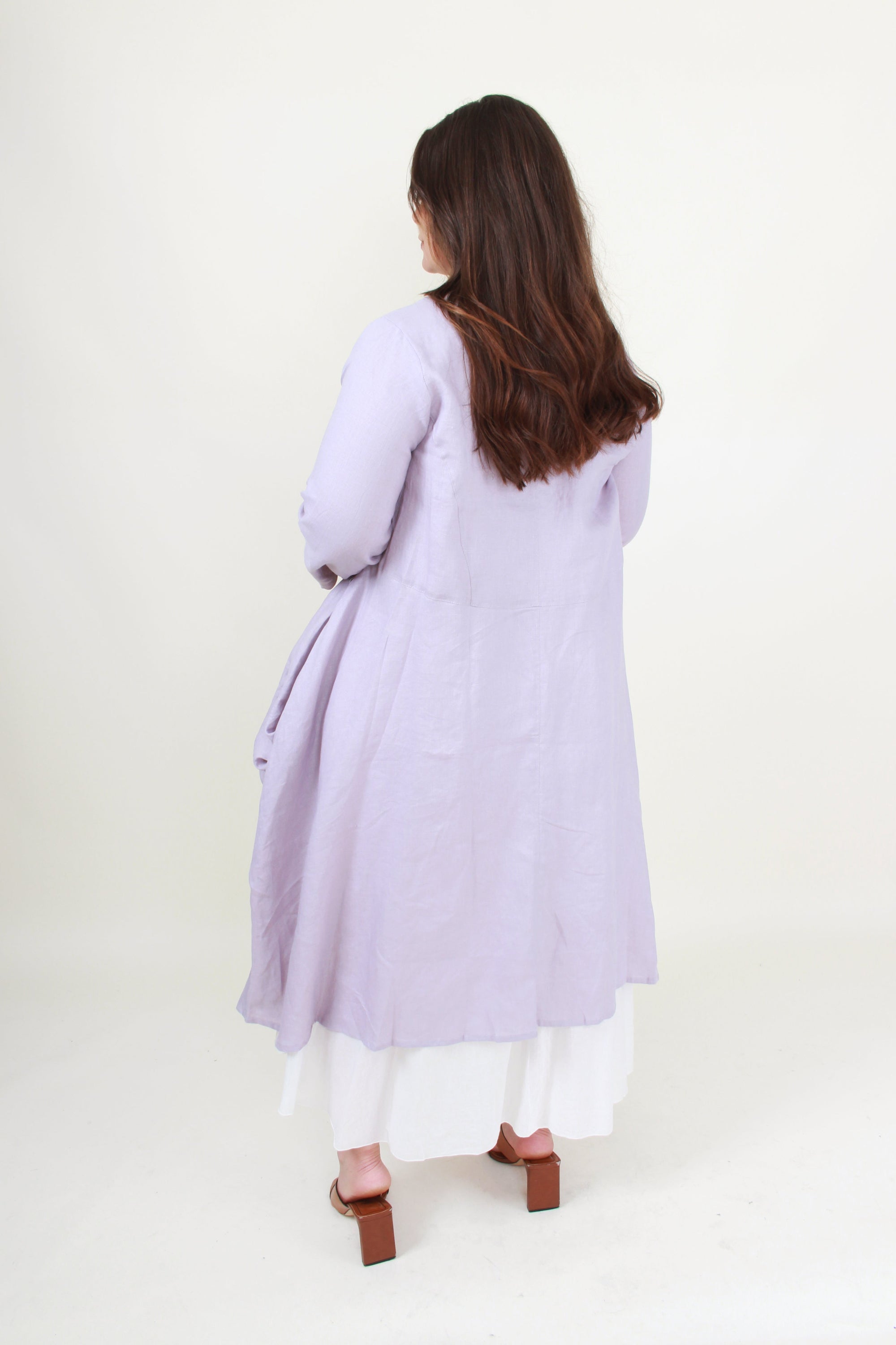 Woman wearing a light purple long dress with white pants on a white background back view