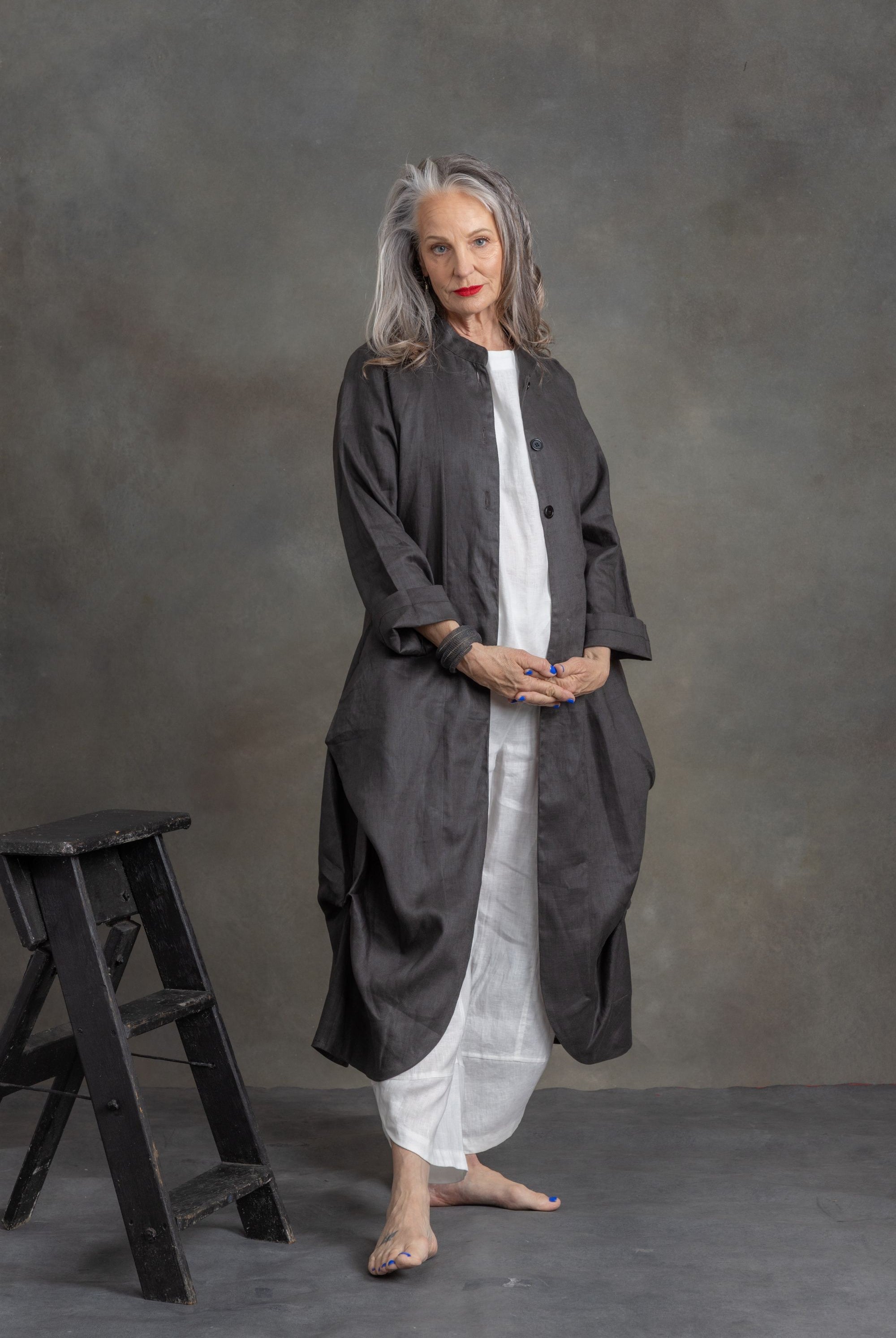 Woman wearing a long dark coat over a white dress against a gray background