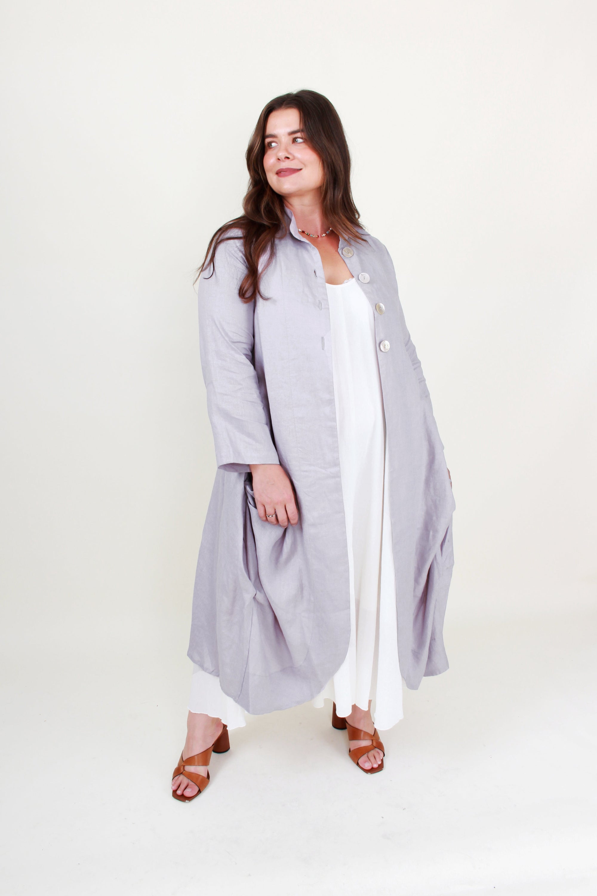 Woman wearing a long light gray coat over a white outfit on a white background