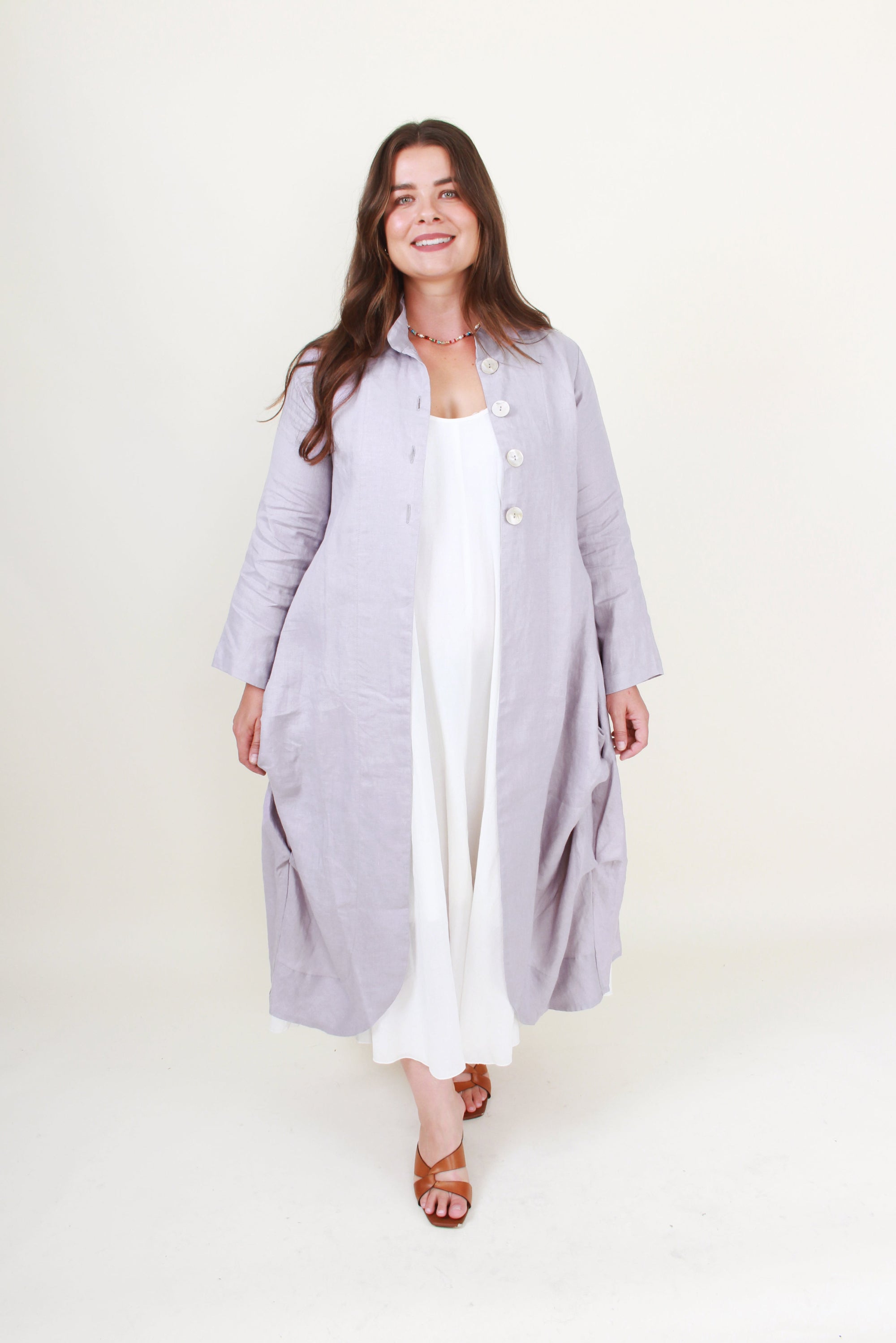 Woman wearing a long light gray coat over a white outfit on a white background