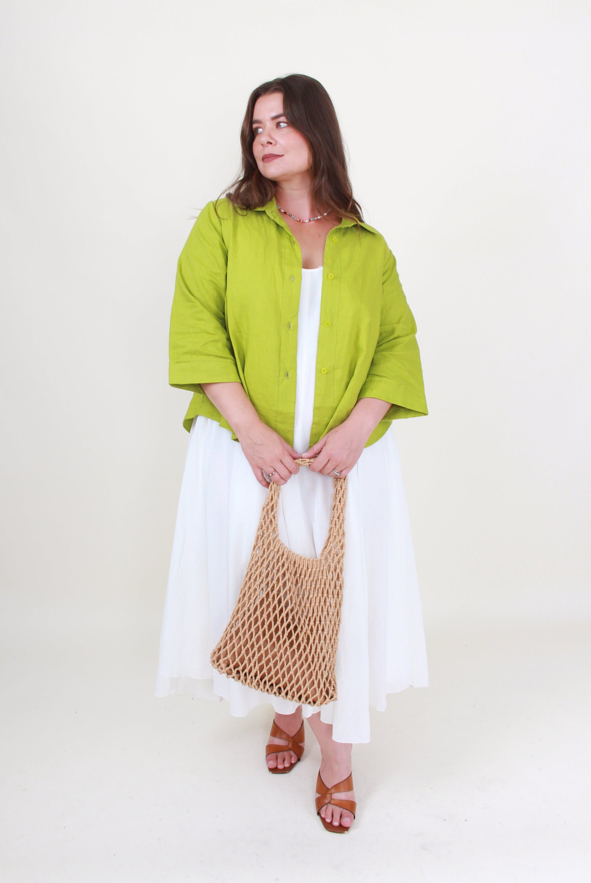 Woman wearing a green jacket and white dress holding a woven bag on a white background