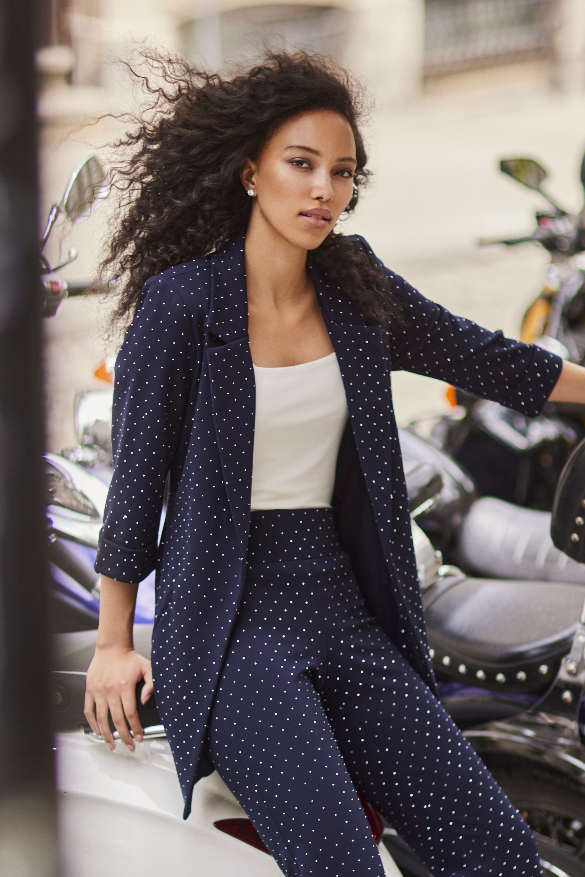 Woman in a navy diamante outfit sitting on a motorcycle in an urban setting