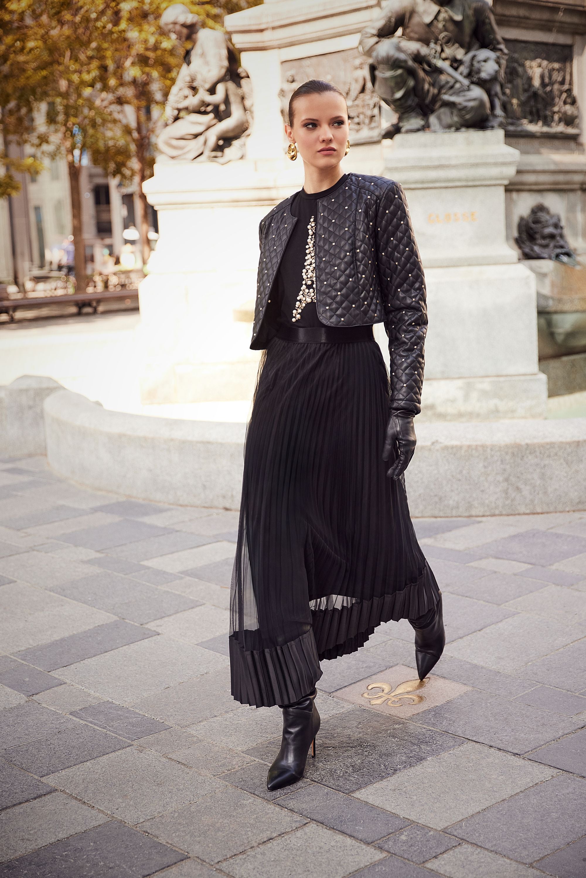 Woman in a black outfit standing in front of a statue in an urban setting