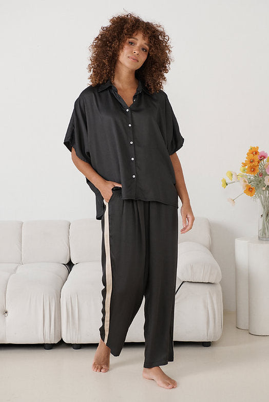 Woman wearing comfortable dark lounge pants with beige side stripe against white lounge background