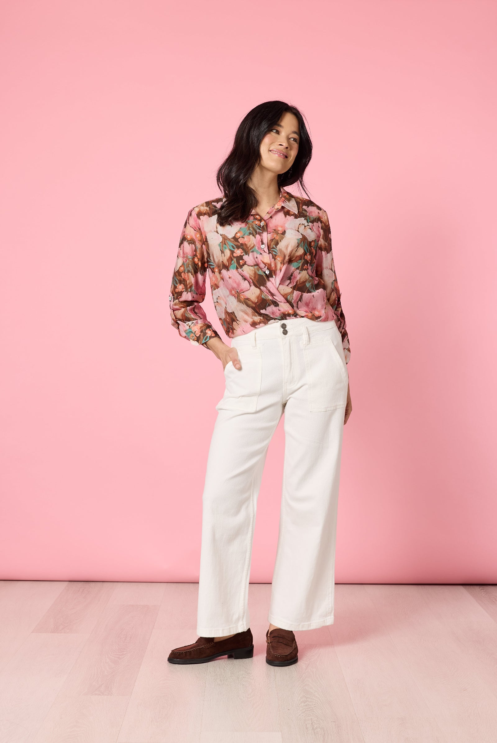 Woman wearing a floral blouse and white pants against a pink background