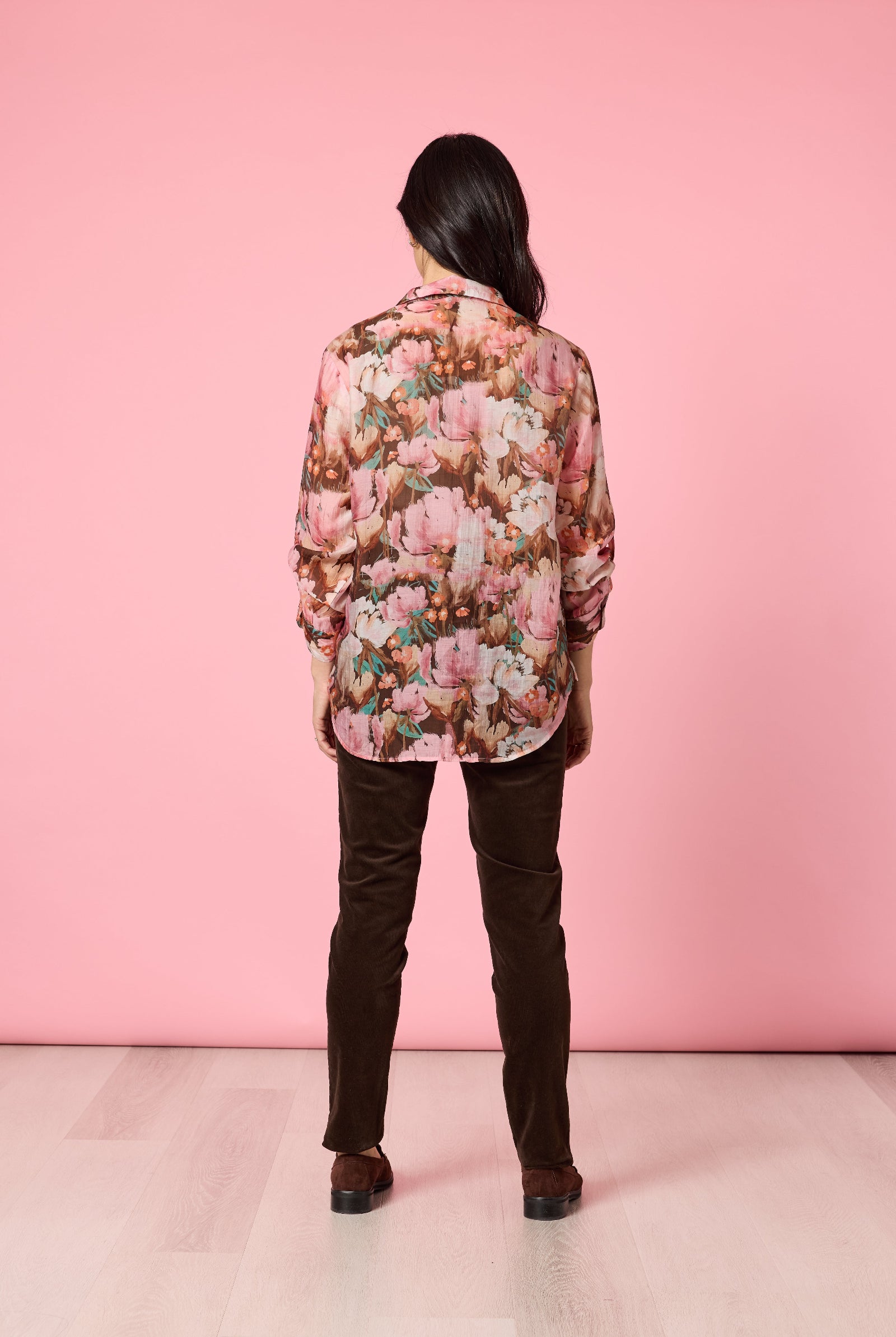 Person wearing a floral blouse and dark pants against a pink background