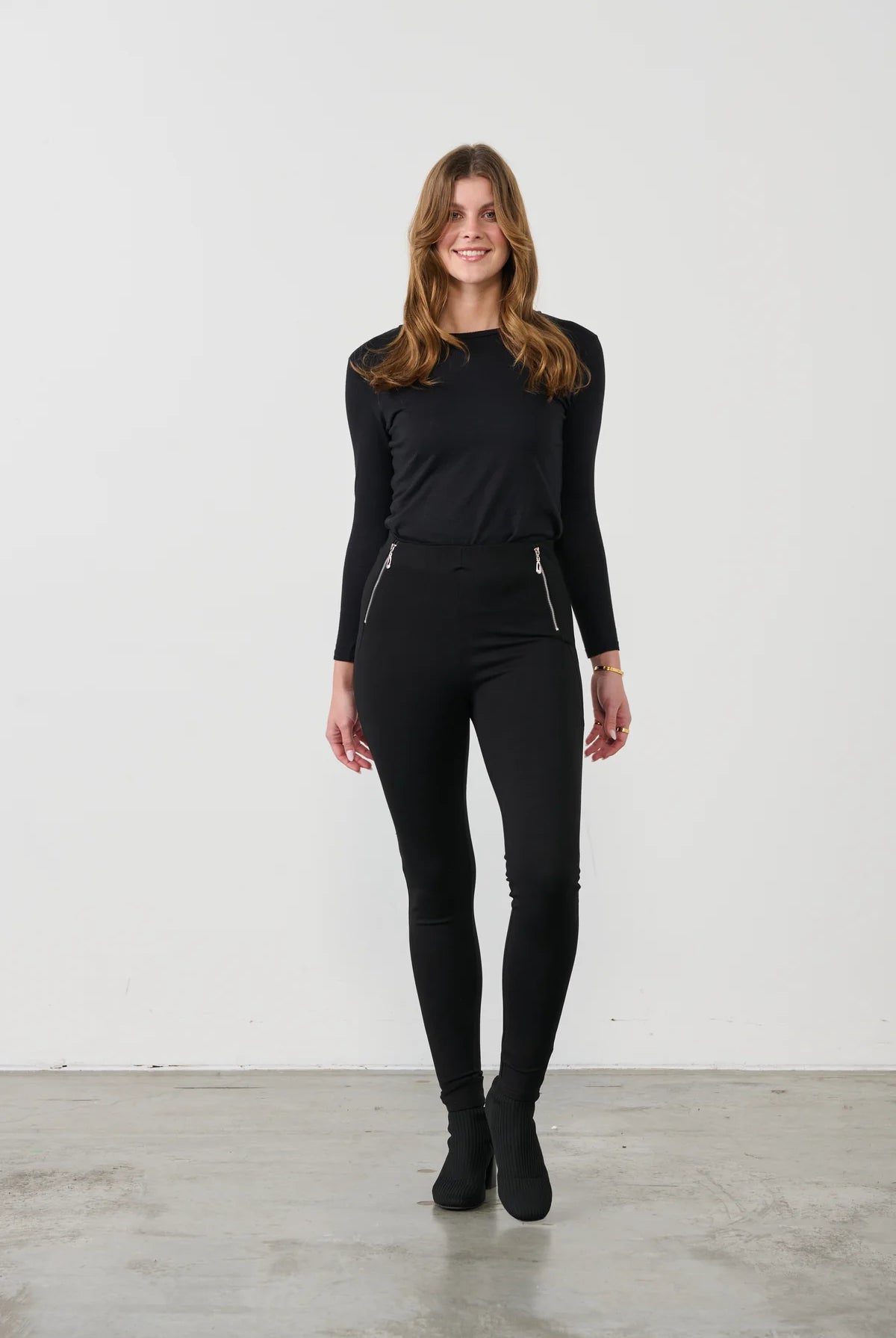 women wearing slim black pants and black top on a white background and gre floor