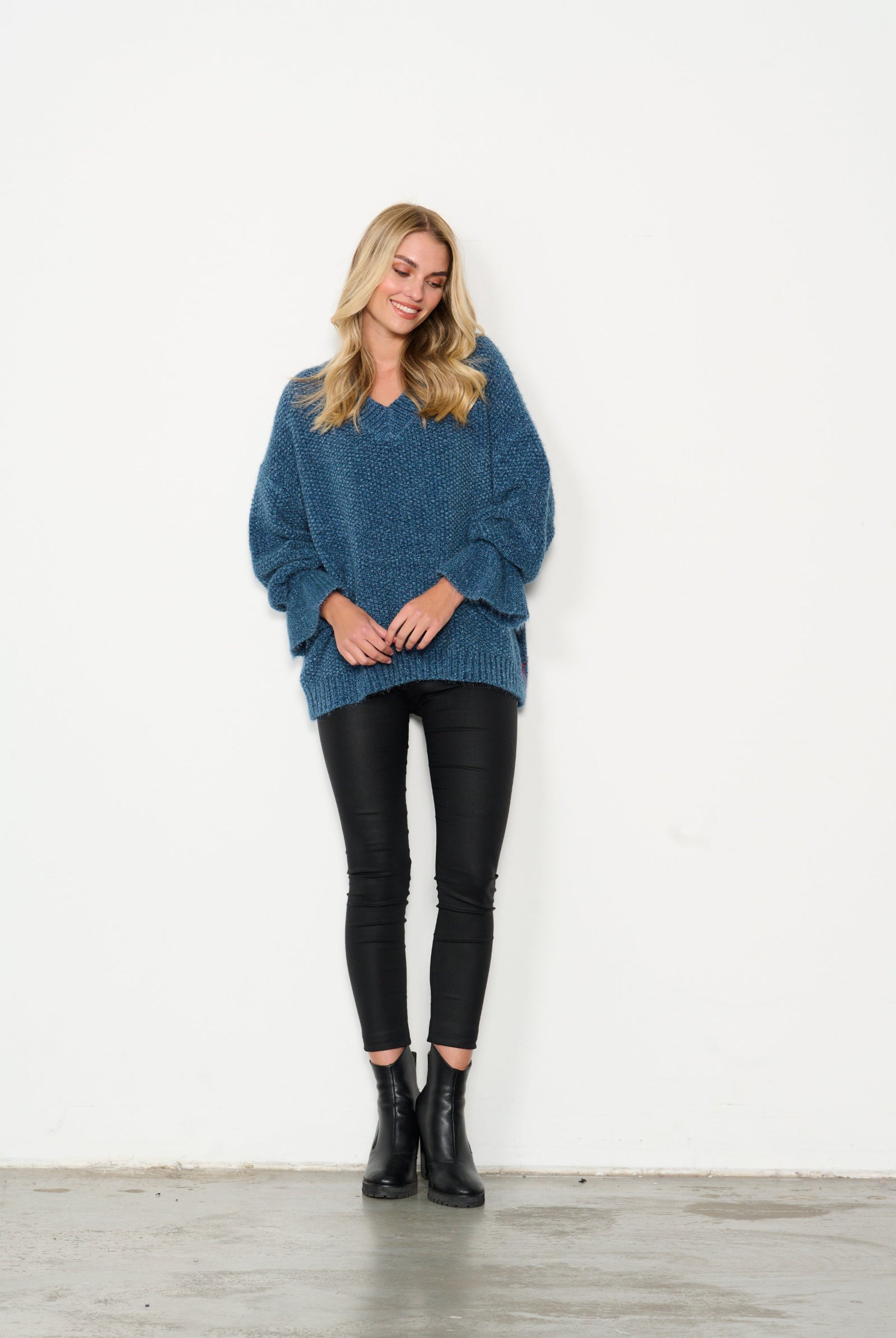 Woman wearing a blue sweater, black leggings, and black boots on a white background