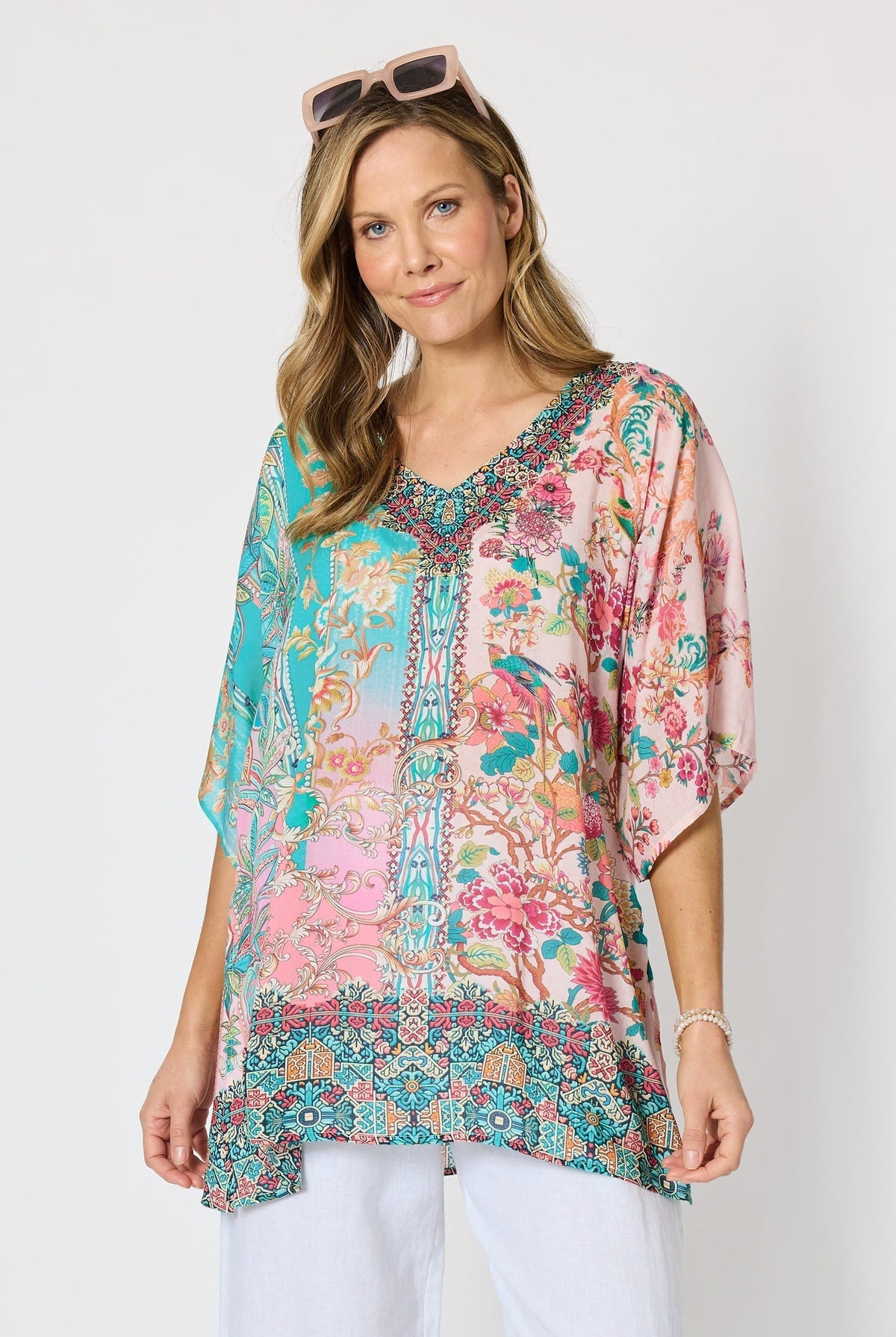 Woman wearing a colourful pink and blue printed floaty top with elbow length sleeves and detailed border and neckline.