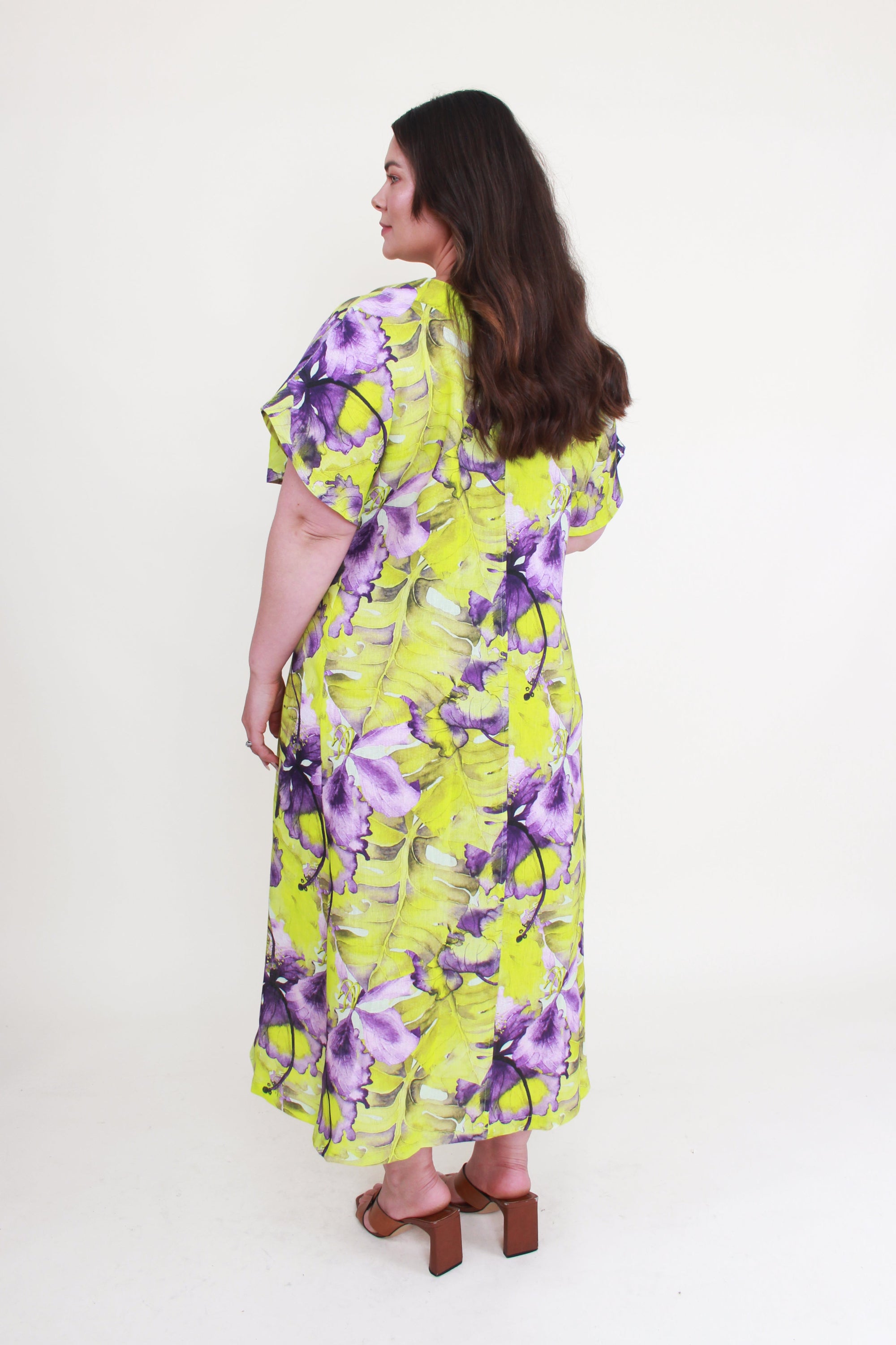 Woman wearing a yellow floral dress on a white background back