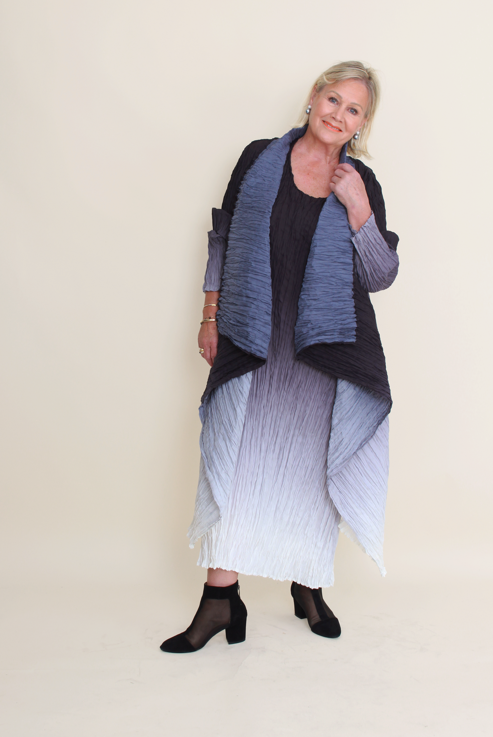 Woman wearing a long, dark blue and gray shawl over a black top and white skirt on a beige background