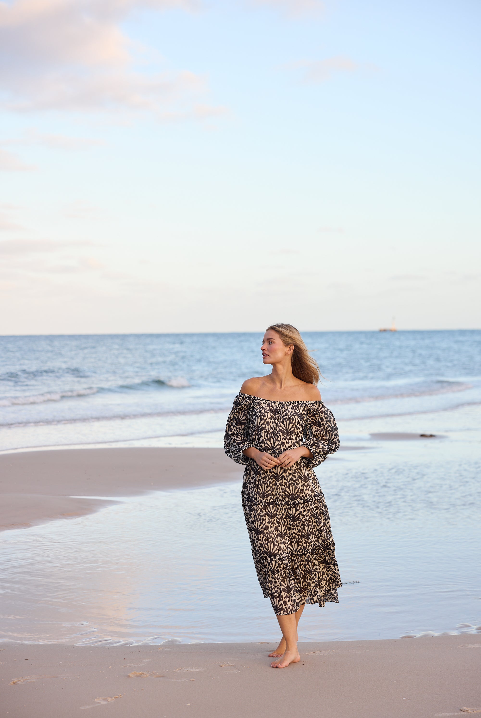 Woman in a floral dress standing on a beach with ocean and sky in the background