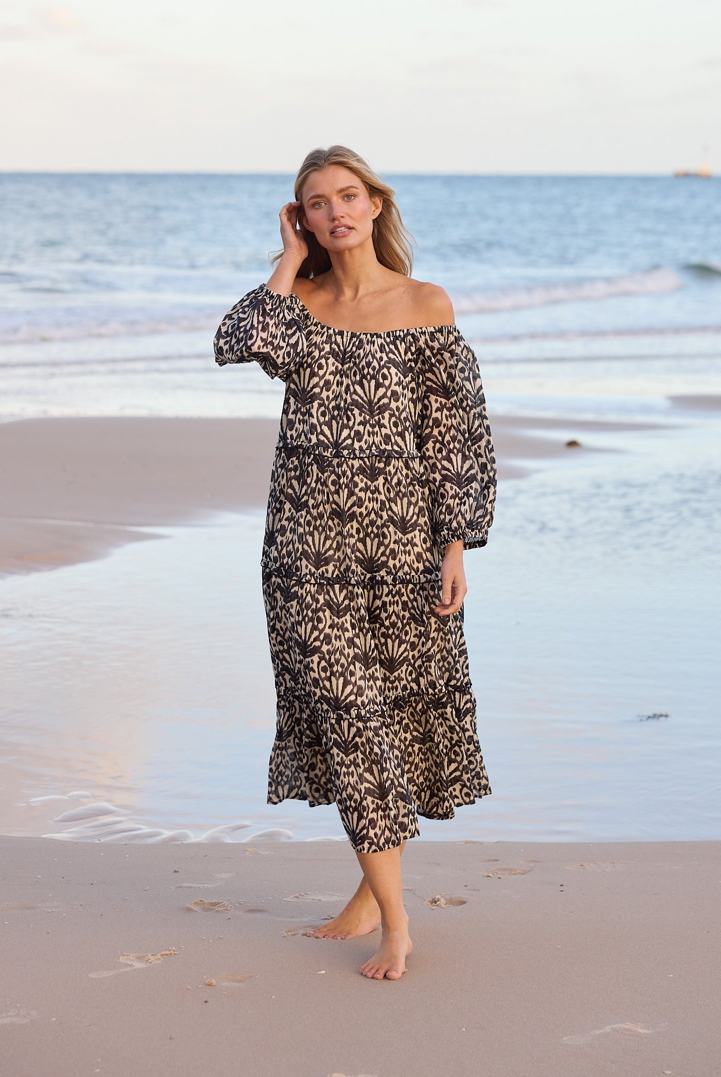 Woman in a patterned dress standing on a beach with ocean waves in the background