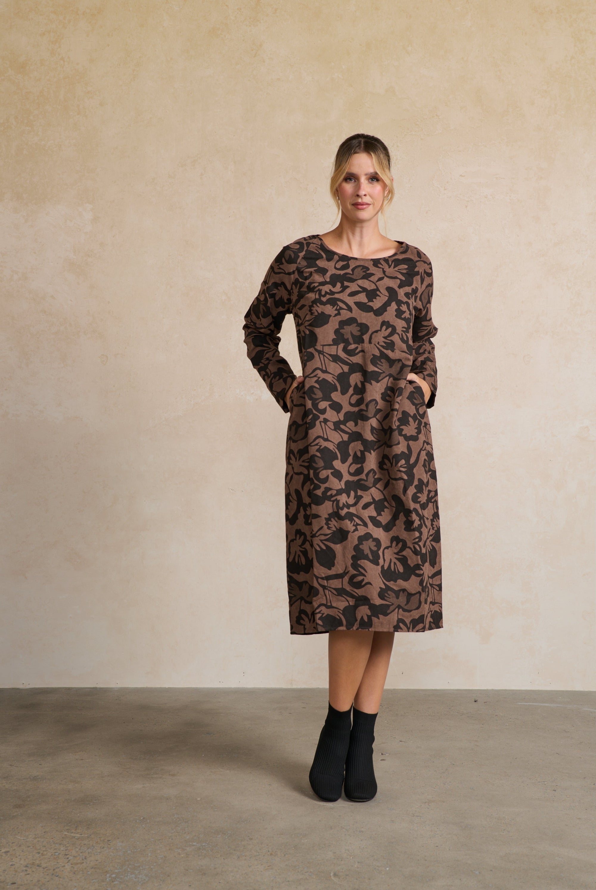 Woman wearing a brown patterned dress against a beige wall.