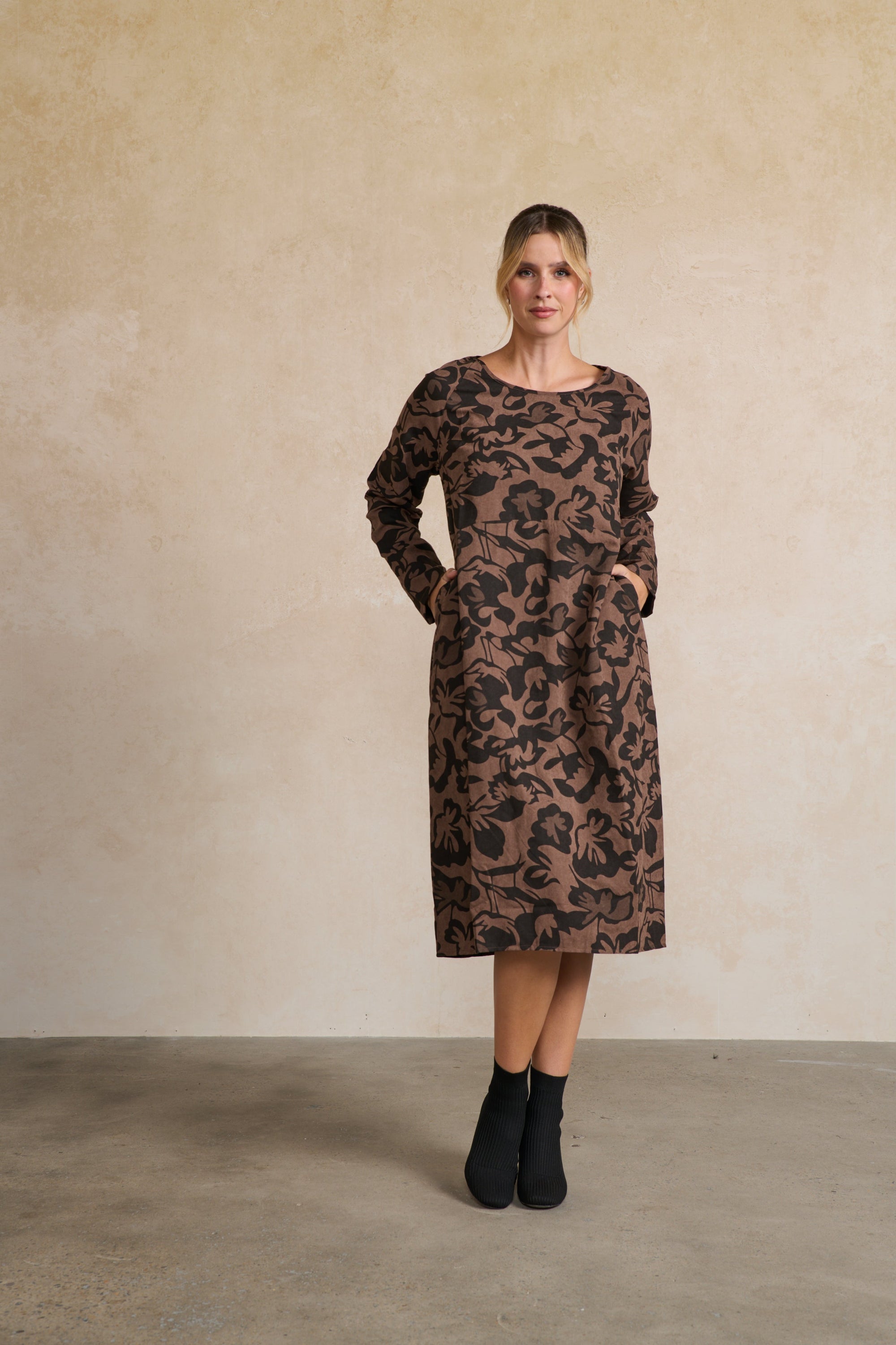 Woman wearing a brown patterned dress against a beige wall.