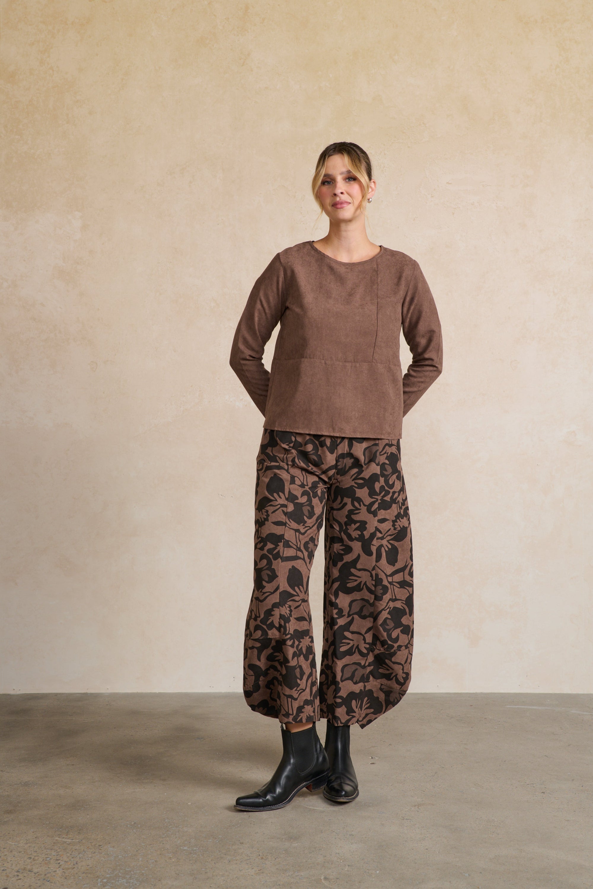 Person wearing a brown top and patterned pants against a beige wall.