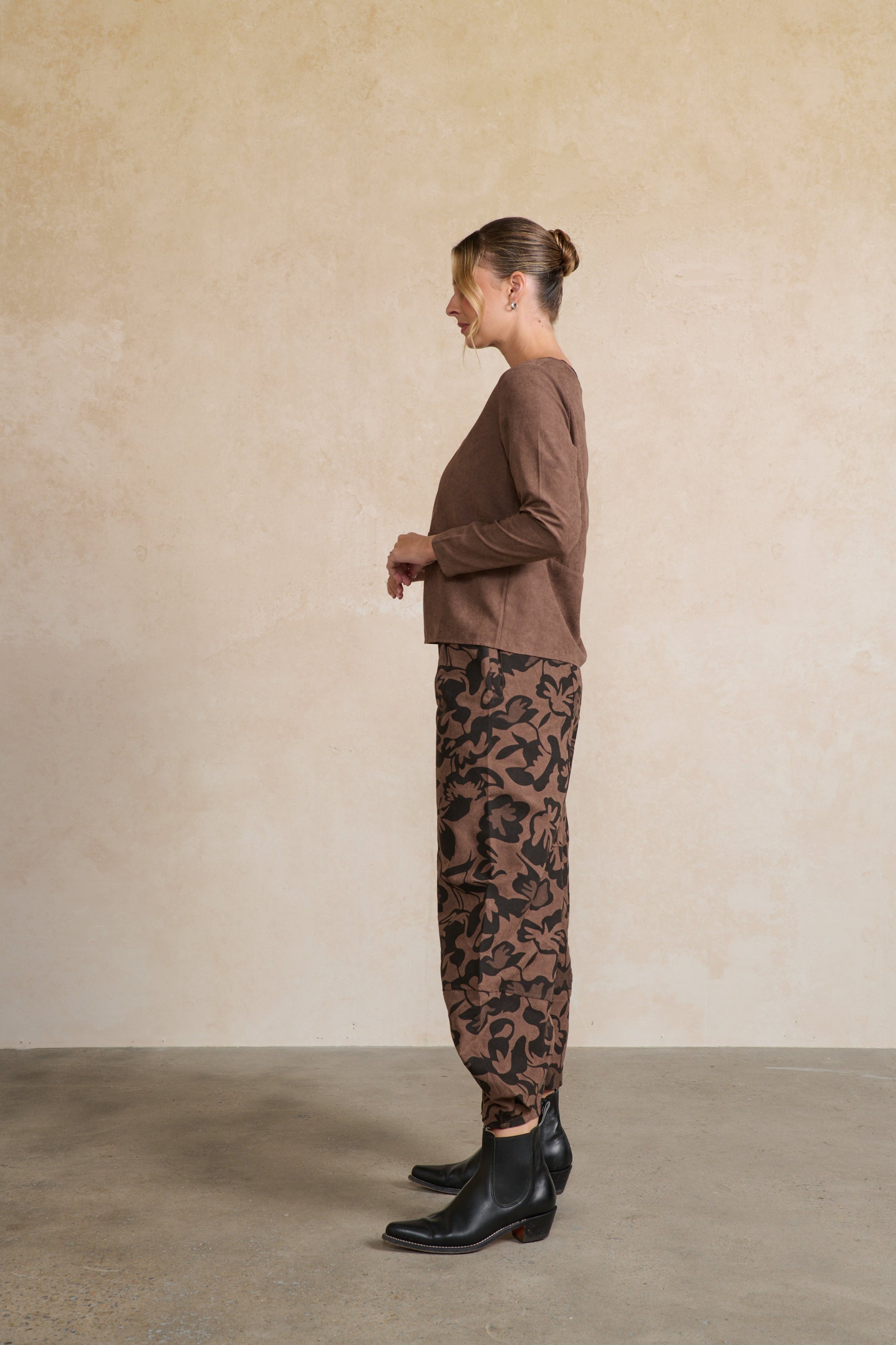 Person wearing a brown top and leopard print pants against a beige wall.