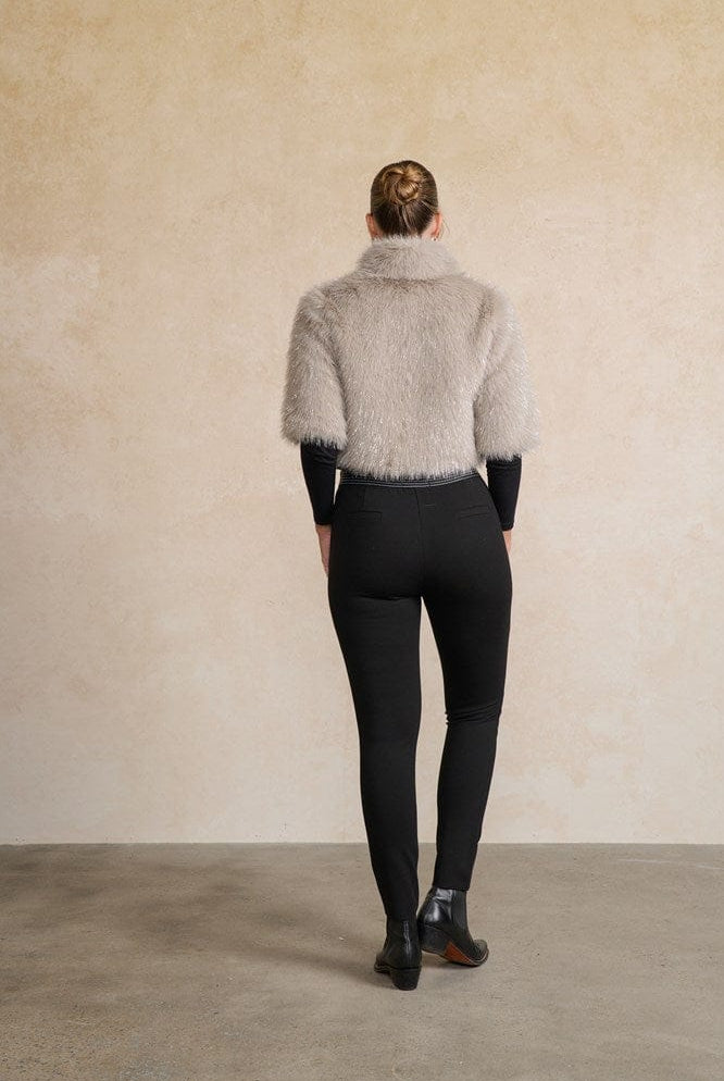 Person wearing a textured gray jacket and black pants against a beige wall back angle