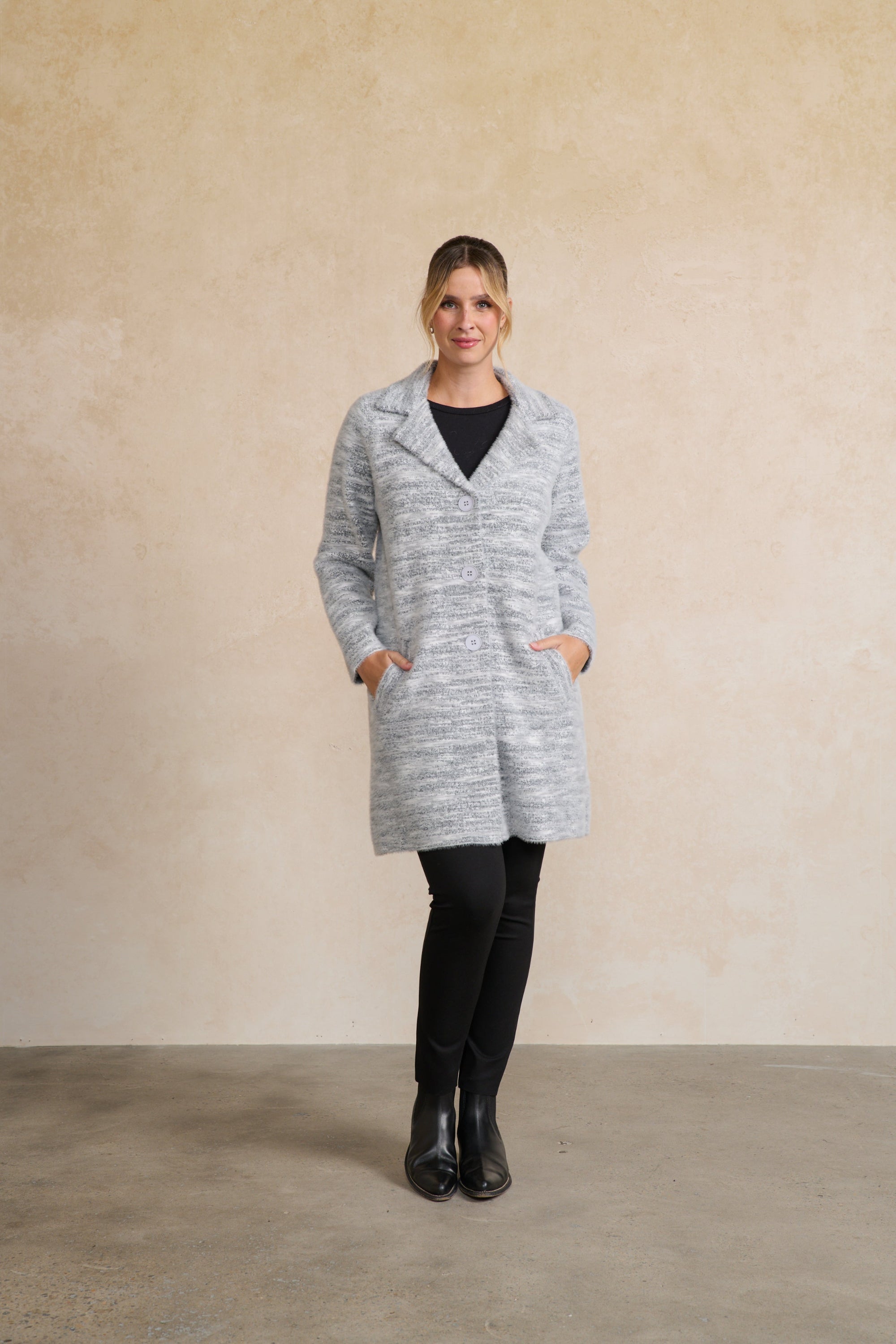 Woman wearing a gray coat standing against a beige wall.