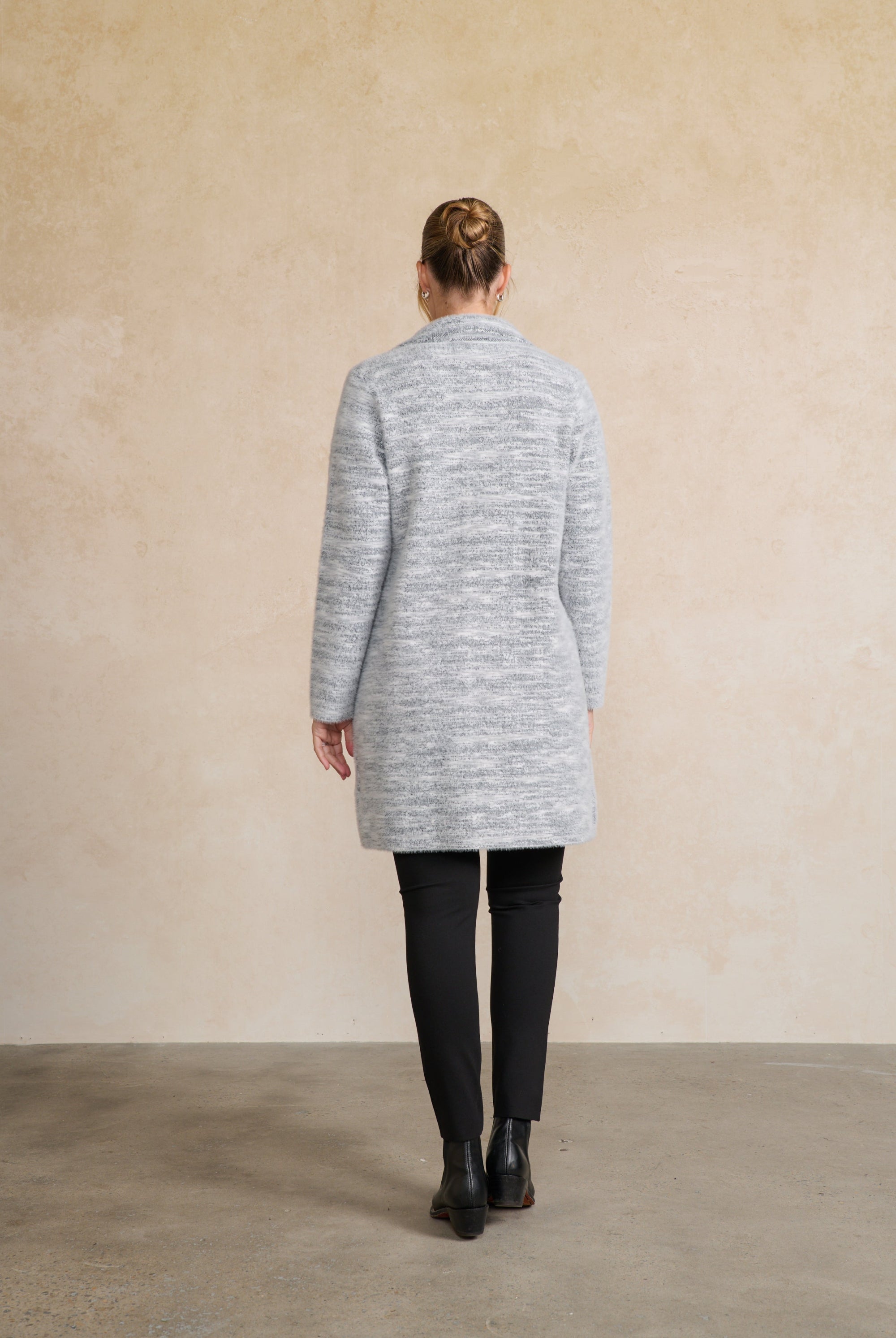 Person wearing a gray cardigan standing against a beige wall back angle